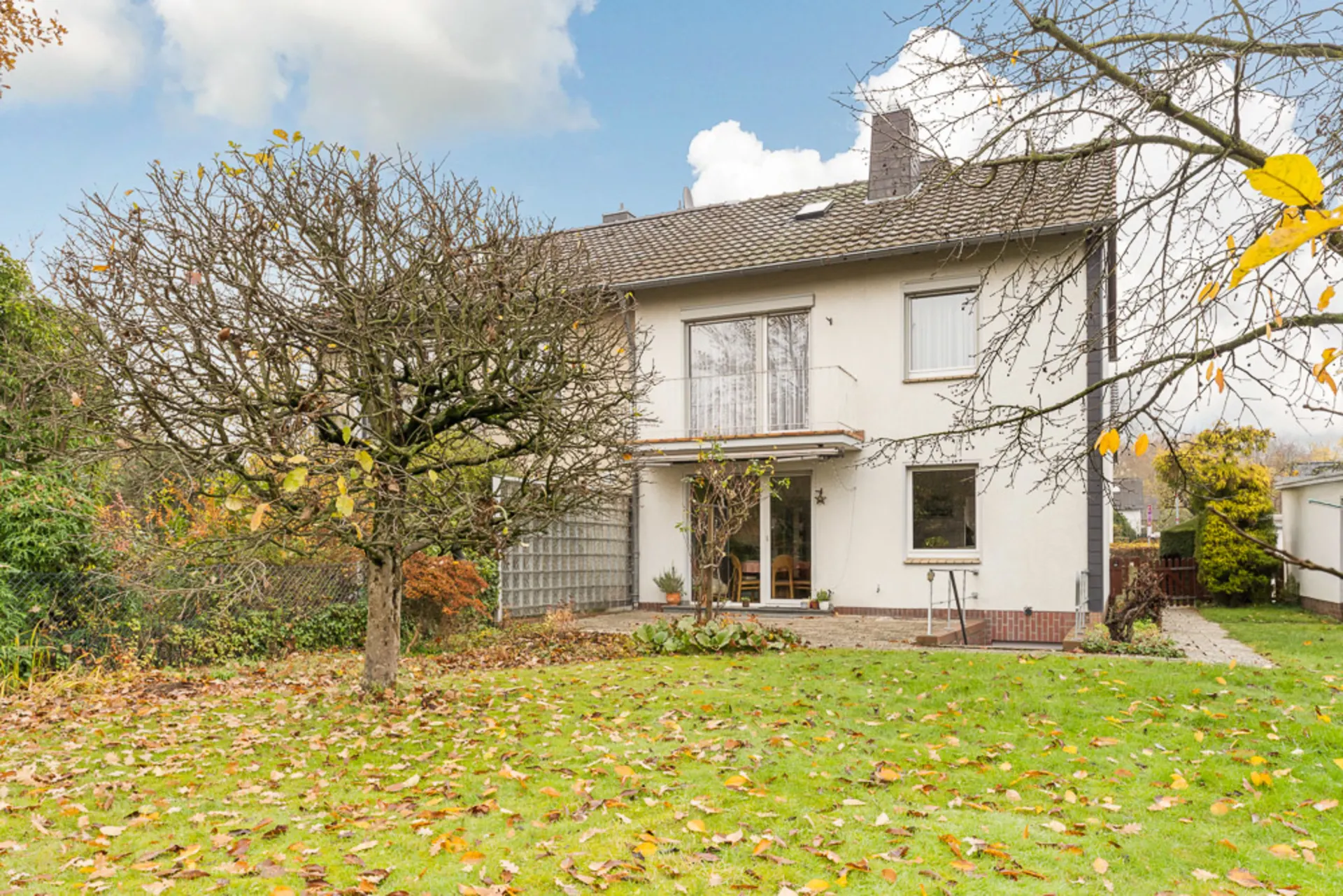 Zweistöckiges Wohnhaus mit Garten, herbstliche Bäume und Rasenfläche im Vordergrund.