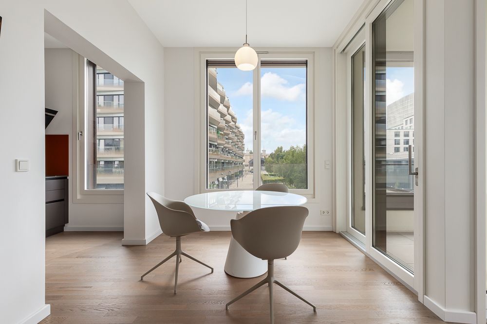 Heller Essbereich mit rundem Tisch, drei Stühlen und großen Fenstern in moderner Wohnung.