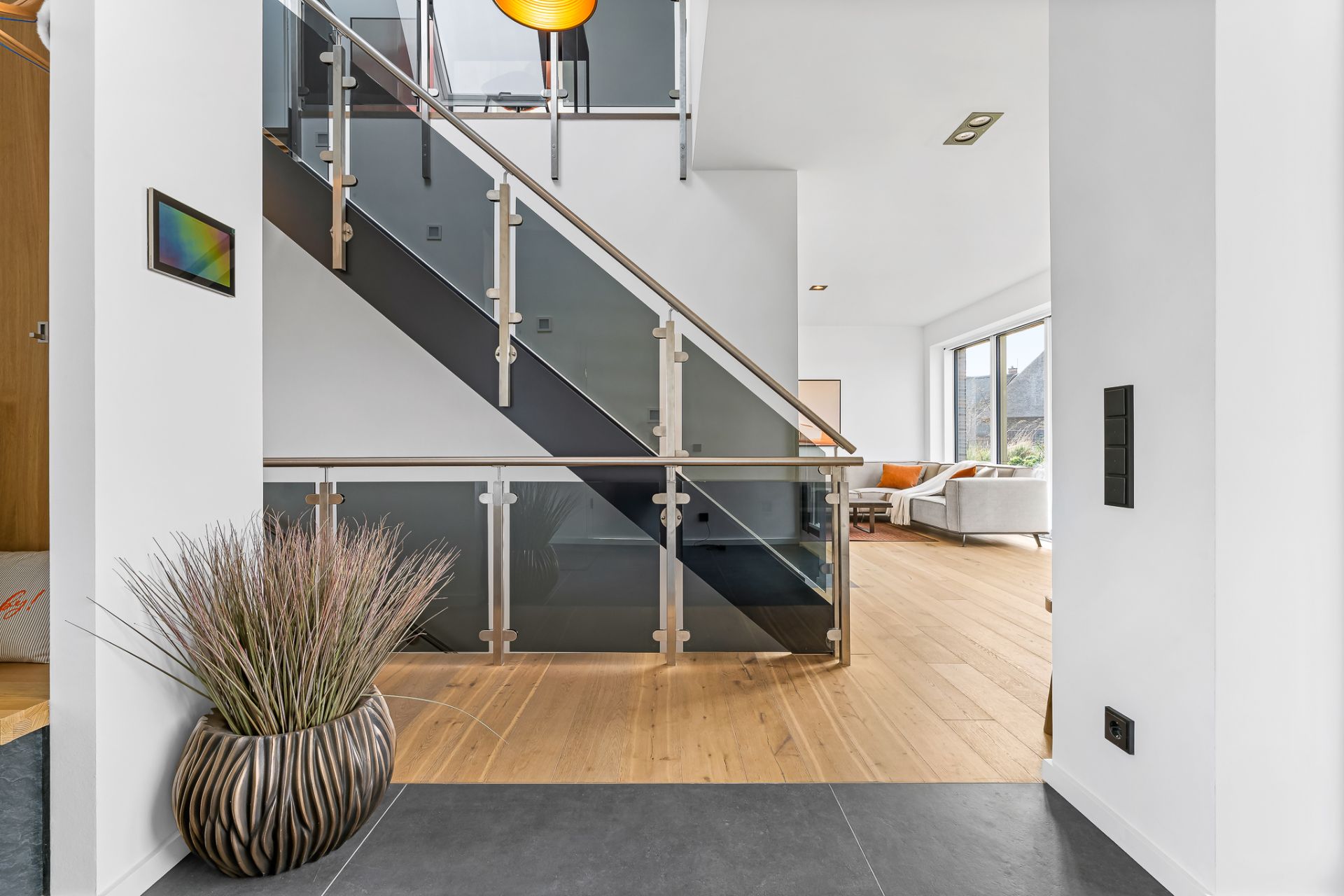 Moderne Treppe mit Glasgeländer und Wohnzimmer mit Sofa im Hintergrund.