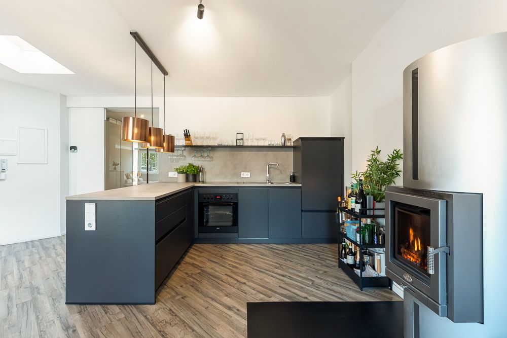 Moderne Küche mit dunklen Schränken, Kochinsel, Holzfußboden und Kamin mit Feuer.