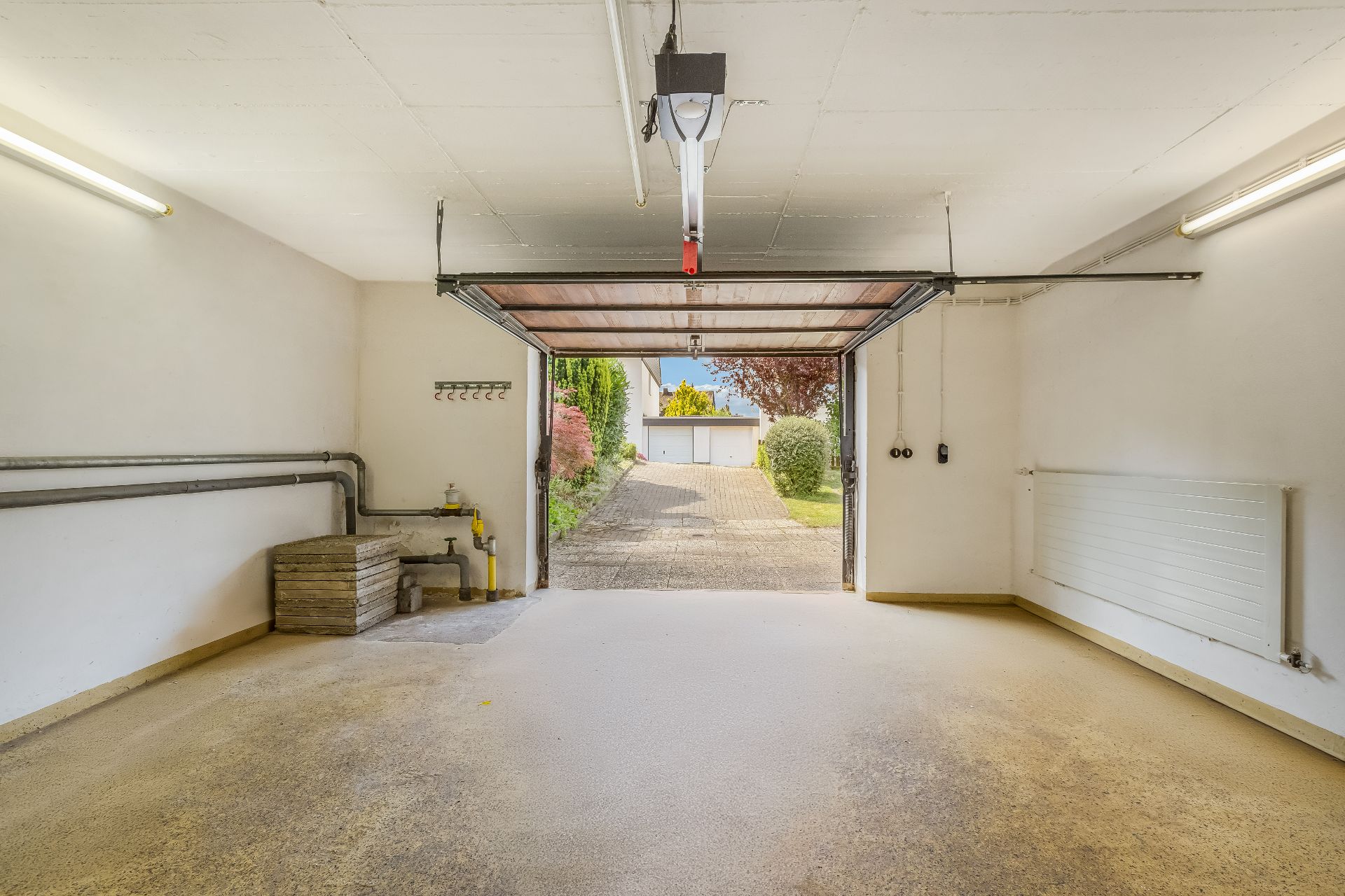 Innenansicht einer sauberen Garage mit offenem Tor und Blick auf eine Einfahrt.