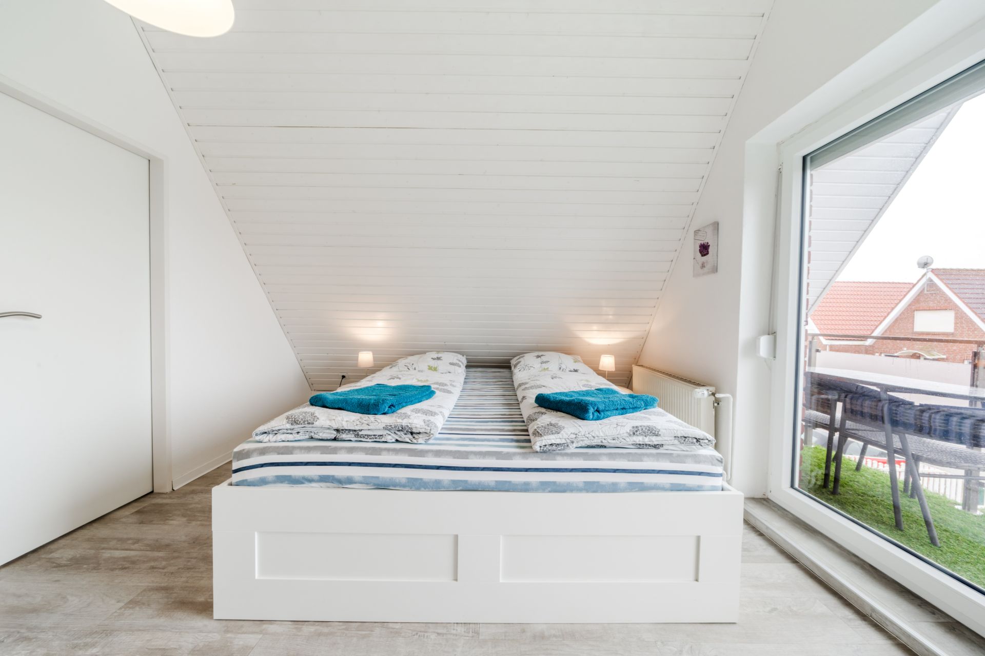 Schlafzimmer mit Doppelbett unter Dachschräge, großer Fensterfront und zwei Nachttischlampen.