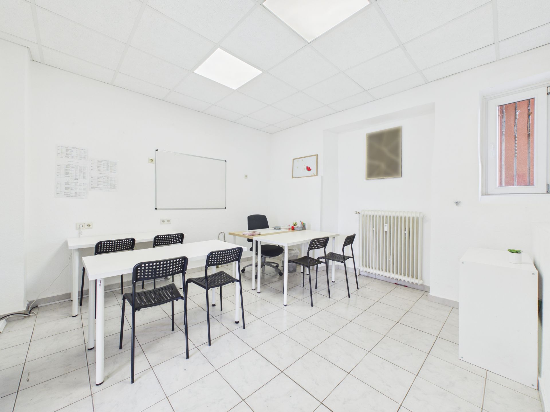 Heller Raum mit weißen Tischen, schwarzen Stühlen und einer Tafel an der Wand.