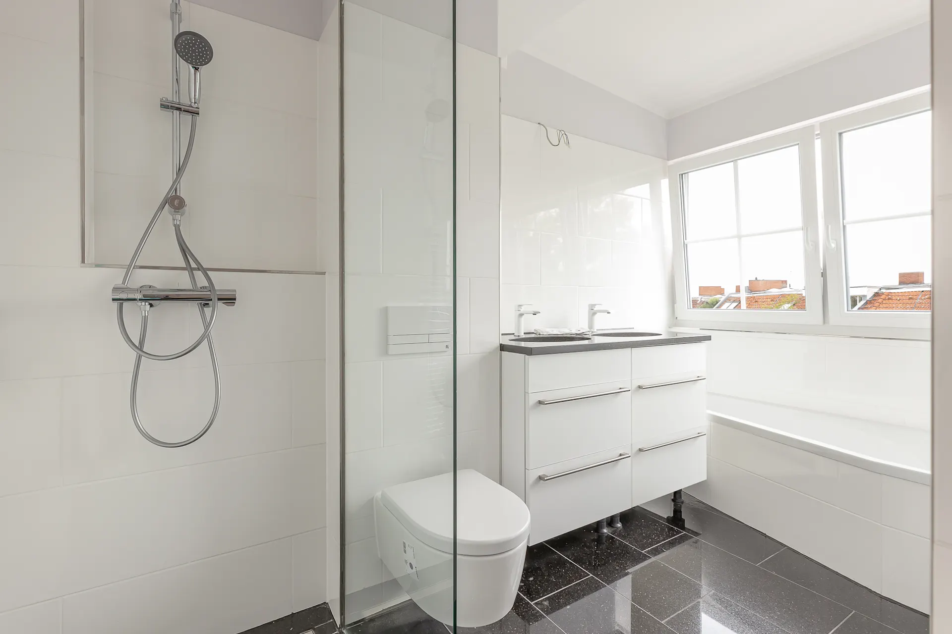 Modernes Badezimmer mit Dusche, WC, Doppelwaschbecken und Badewanne unter einem Fenster.