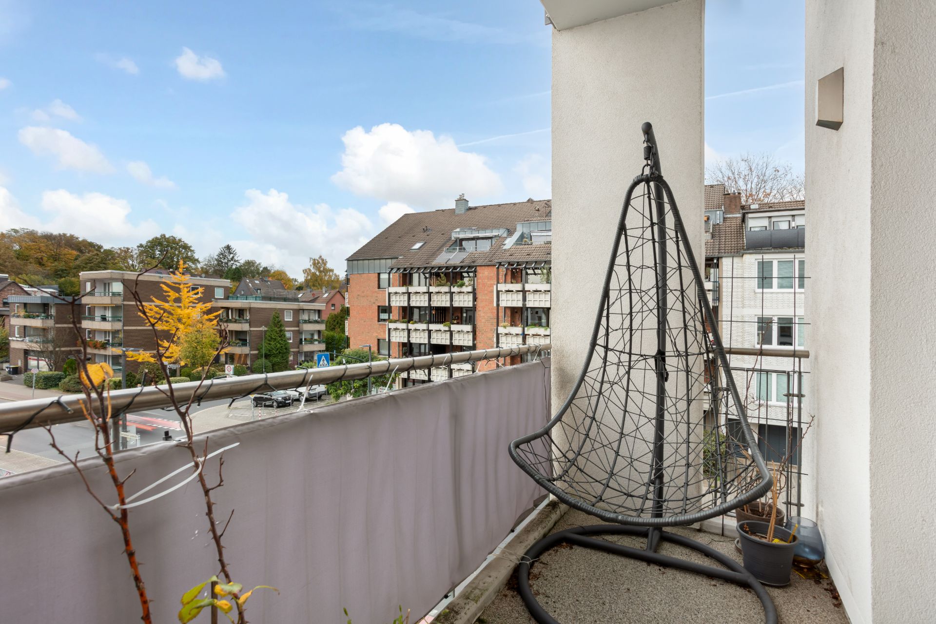 Balkon mit hängendem Stuhl und Pflanze, Blick auf Wohnhäuser und Straße.