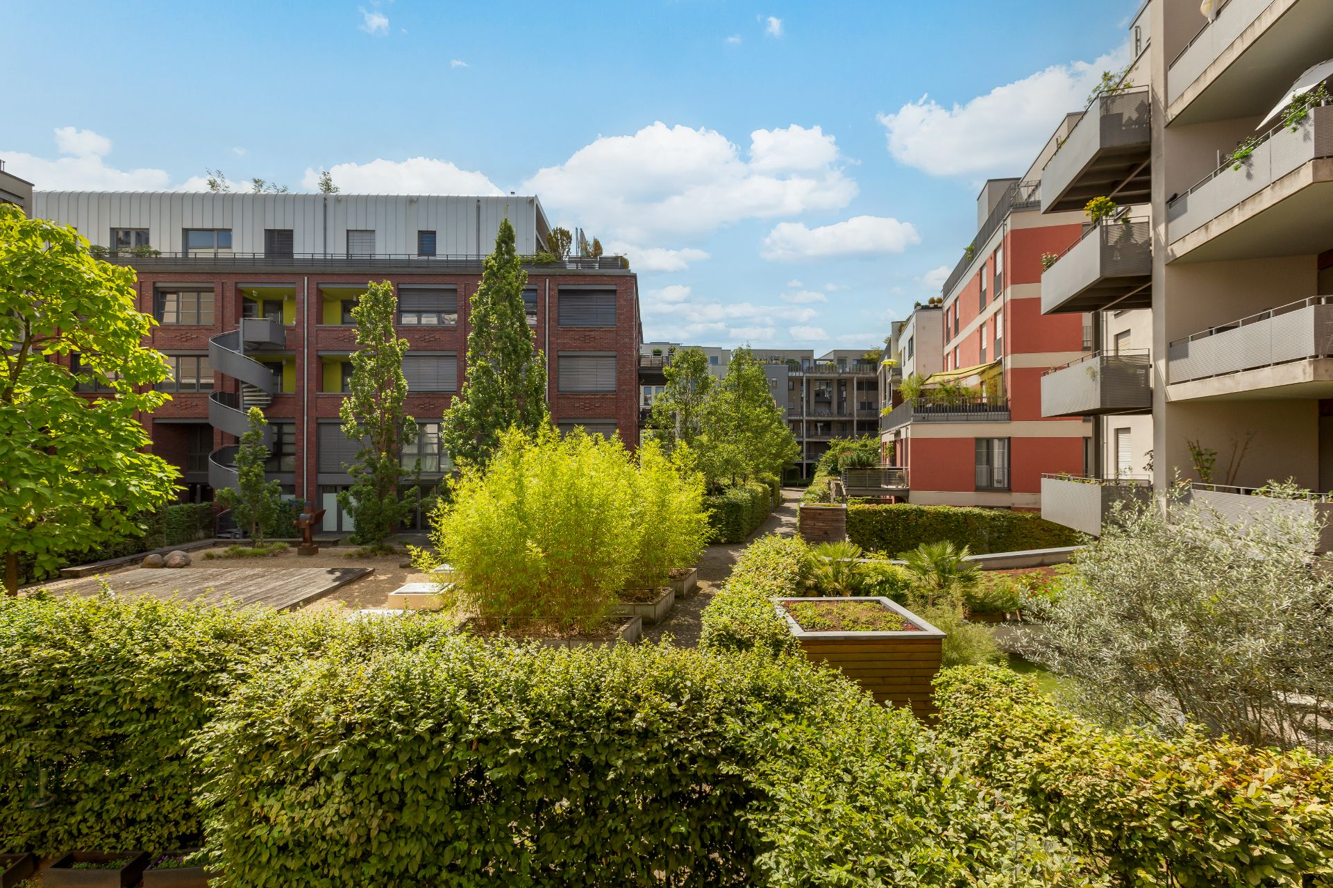 Innenhof moderner Wohngebäude mit grünen Büschen, Bäumen und großen Balkonen.
