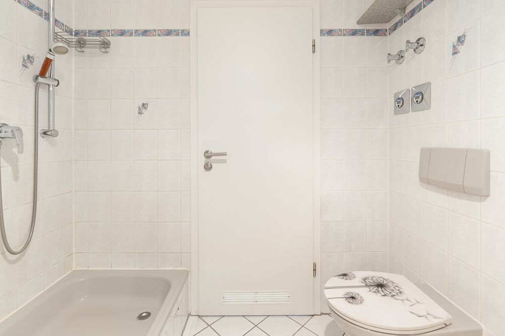 Helles Badezimmer mit Dusche, WC und weiß gefliesten Wänden.
