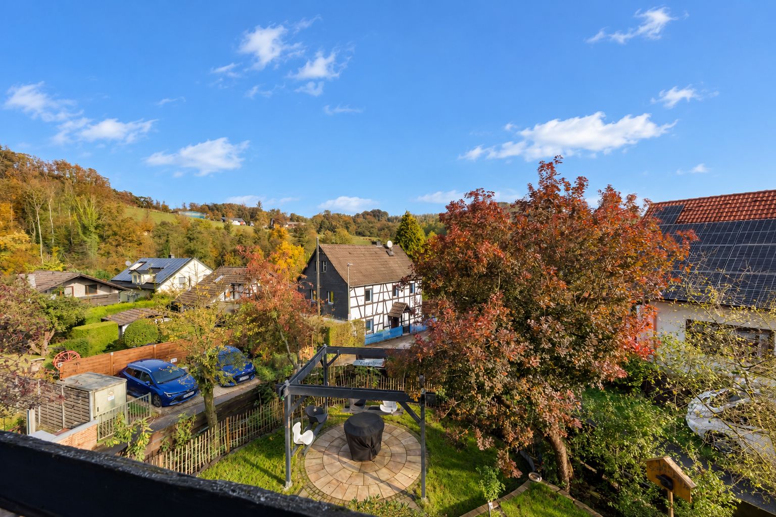 Blick auf einen Garten mit Pavillon, Bäumen und angrenzenden Wohnhäusern bei sonnigem Wetter.