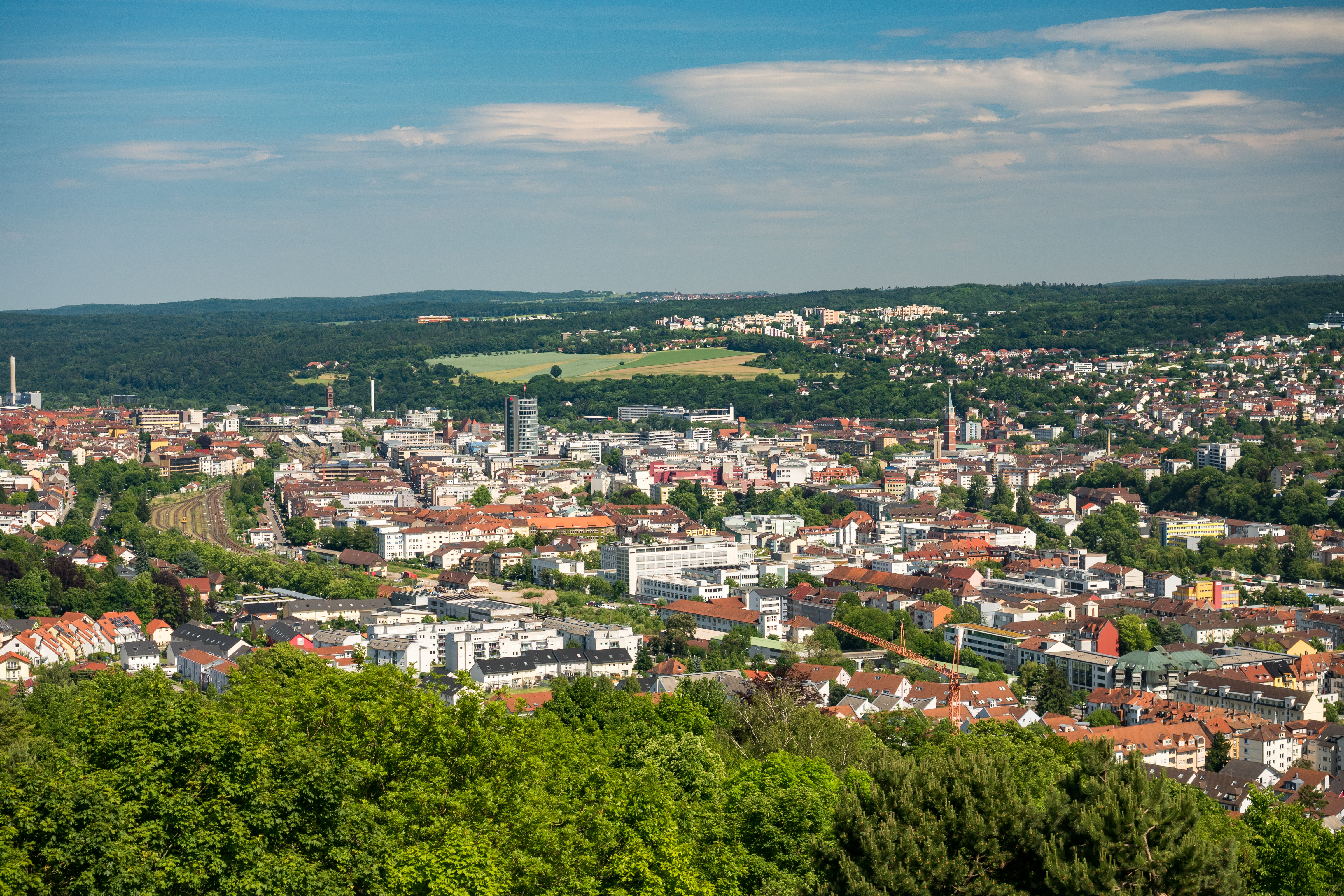 Panoramablick auf eine Stadt mit vielen Häusern und grünen Bäumen im Vordergrund.