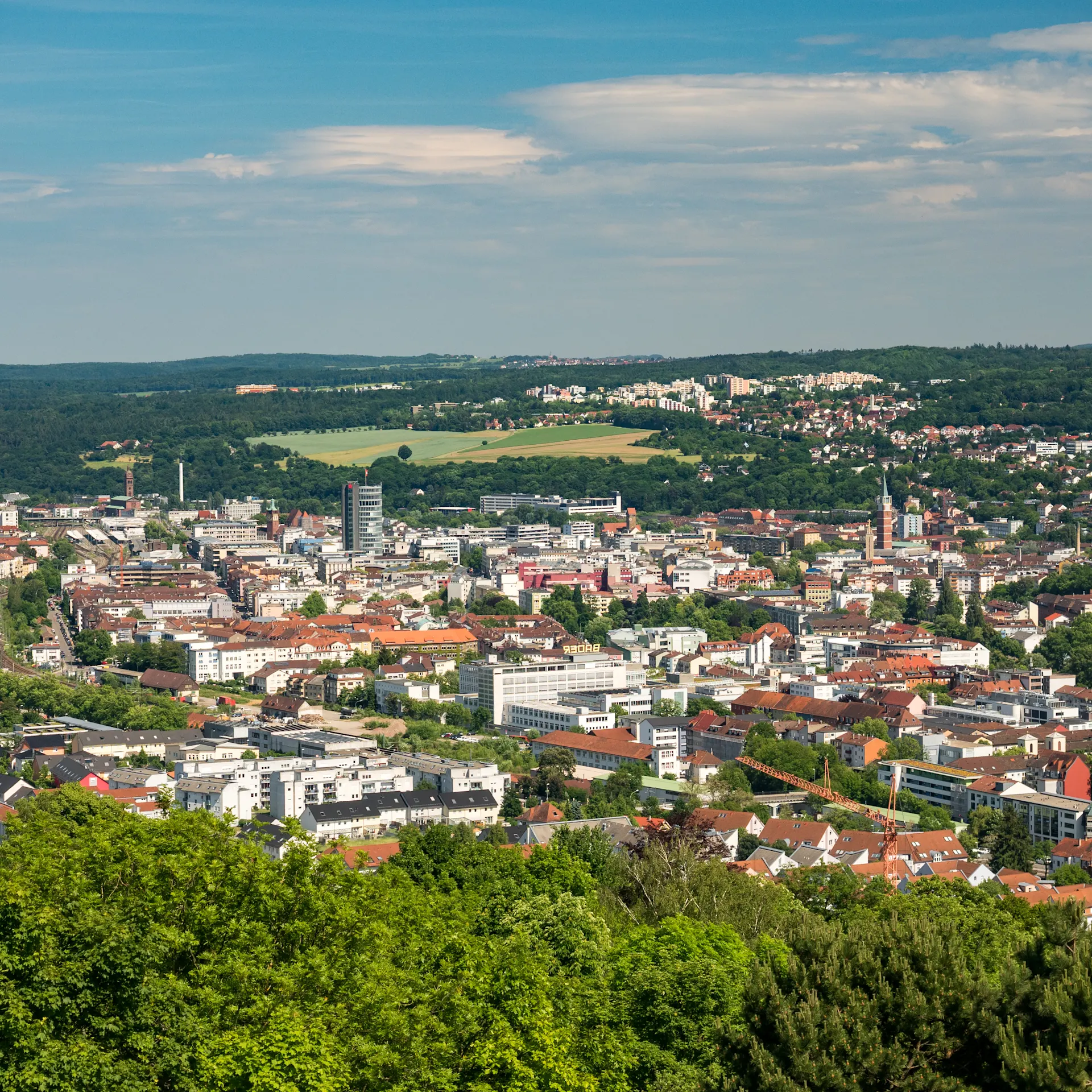 Panoramablick auf eine Stadt mit vielen Häusern und grünen Bäumen im Vordergrund.
