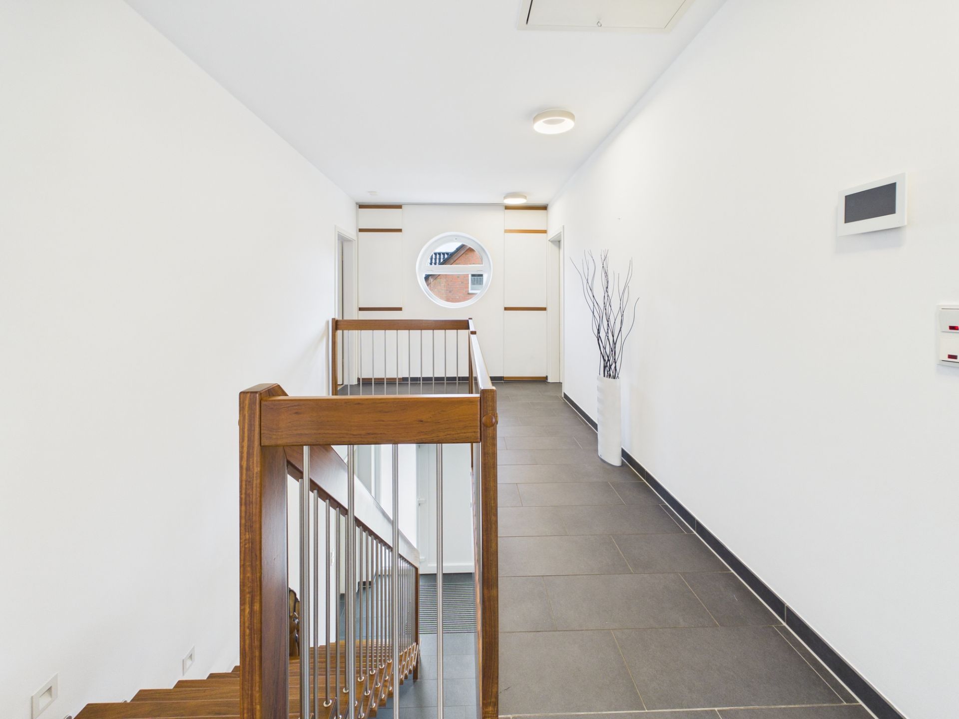 Heller Flur mit Treppe, runden Fenster und Dekovase an der Wand.
