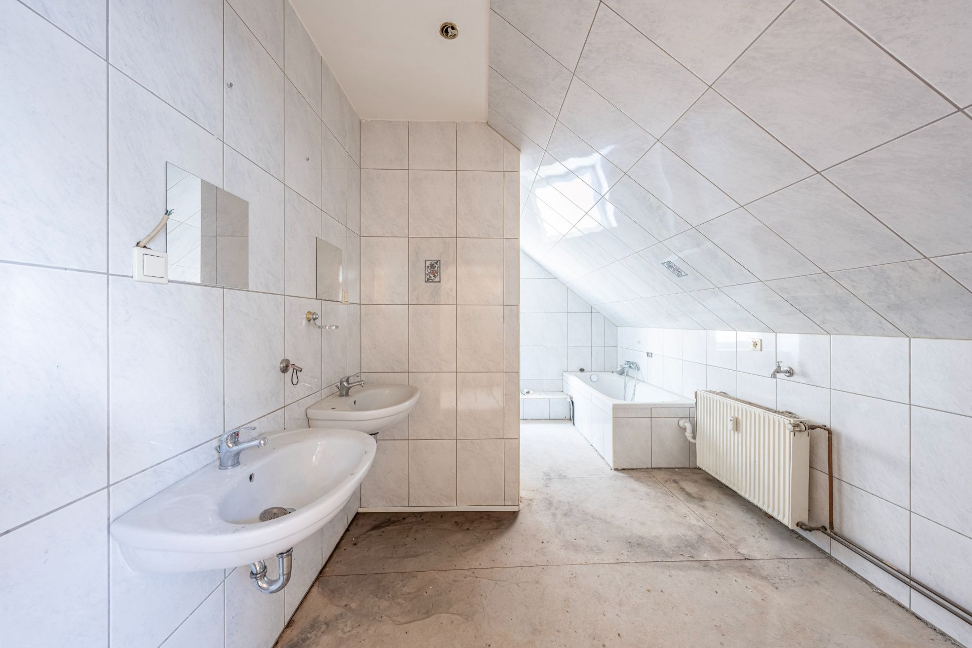 Helles Badezimmer mit zwei Waschbecken, Badewanne und schräger Decke.