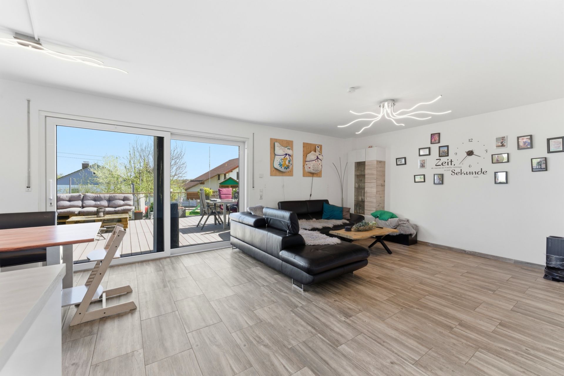 Helles Wohnzimmer mit schwarzem Sofa, Wandbildern und Zugang zur Terrasse.