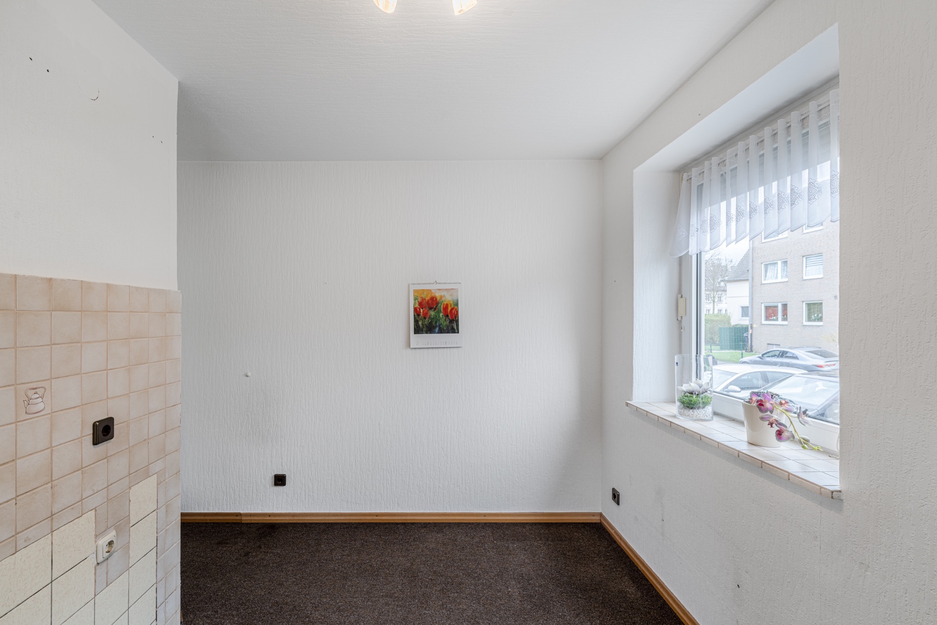 Heller, leerer Raum mit Fenster, Fliese an der Wand und Blumen auf der Fensterbank.