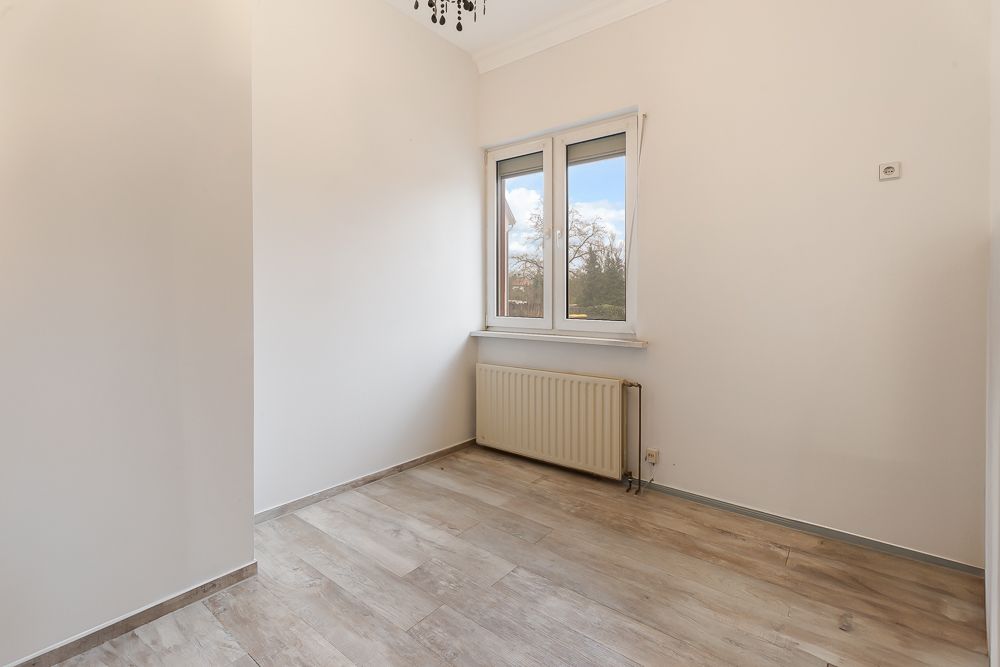 Leerer heller Raum mit Holzfußboden, Fenster und Heizkörper unter dem Fenster.