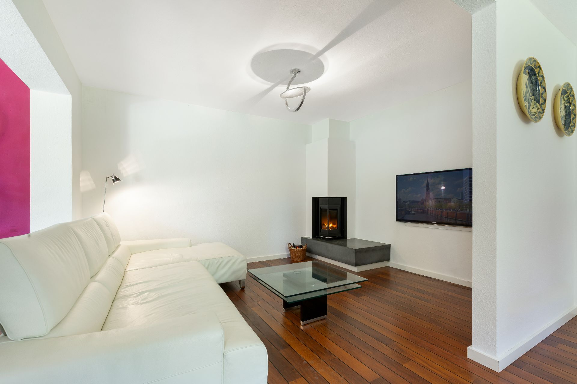 Wohnzimmer mit weißem Sofa, Glastisch, Kamin und Holzfußboden.