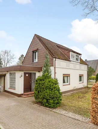 Einfamilienhaus mit Satteldach, Carport und Auto daneben, umgeben von Bäumen und Hecken.