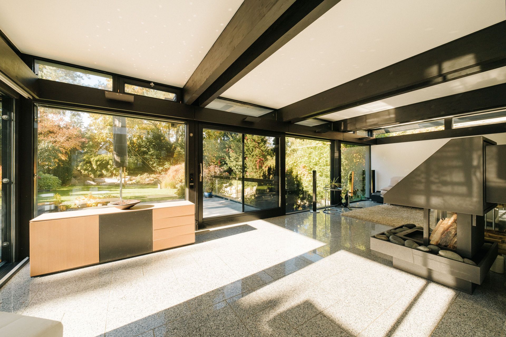 Modernes Wohnzimmer mit großen Fenstern, Kamin und Blick in einen grünen Garten.