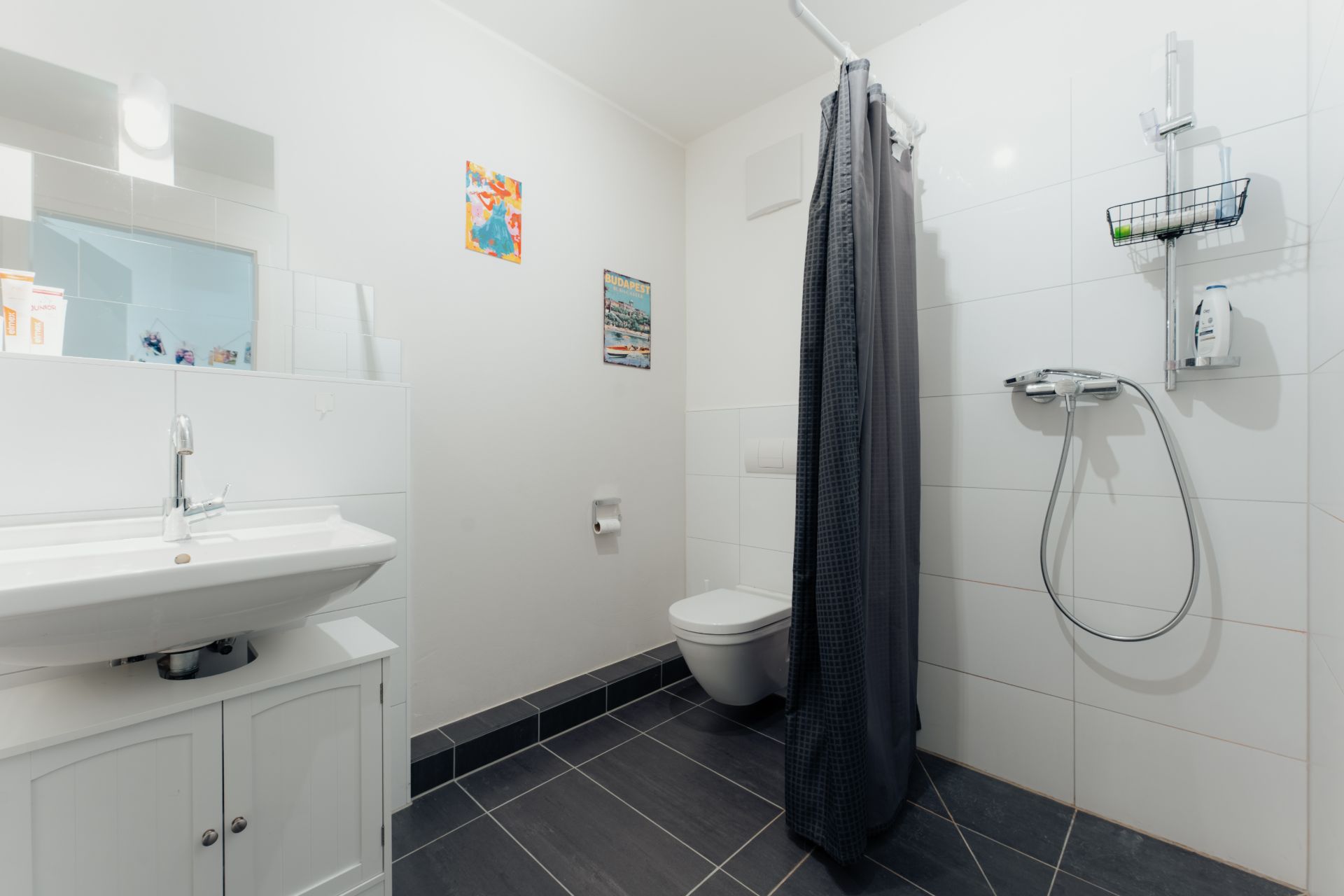 Modernes Badezimmer mit Dusche, WC, Waschbecken und dunklen Bodenfliesen.