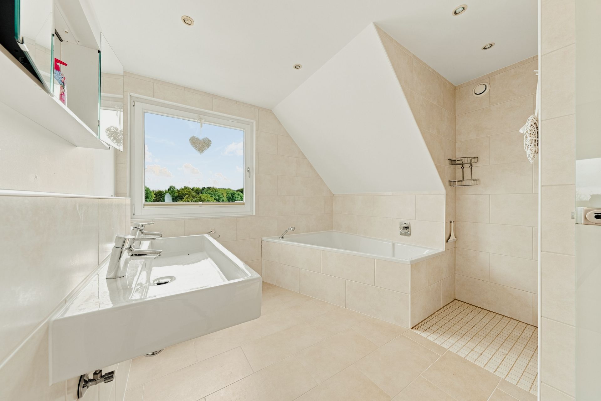 Helles Badezimmer mit großem Fenster, Waschbecken, Badewanne und bodengleicher Dusche.