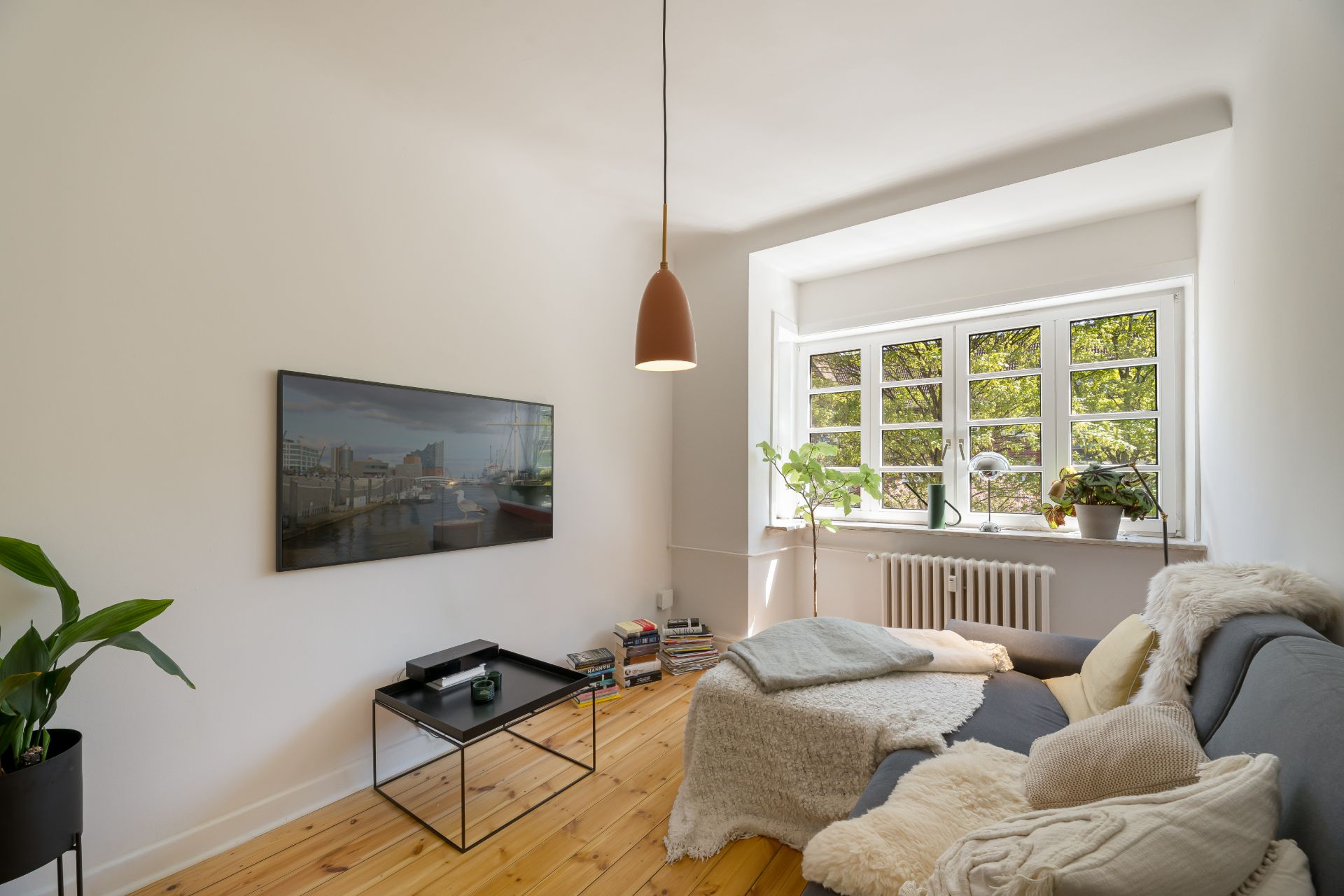 Helles Wohnzimmer mit Sofa, Couchtisch, Pflanzen und großem Fenster.