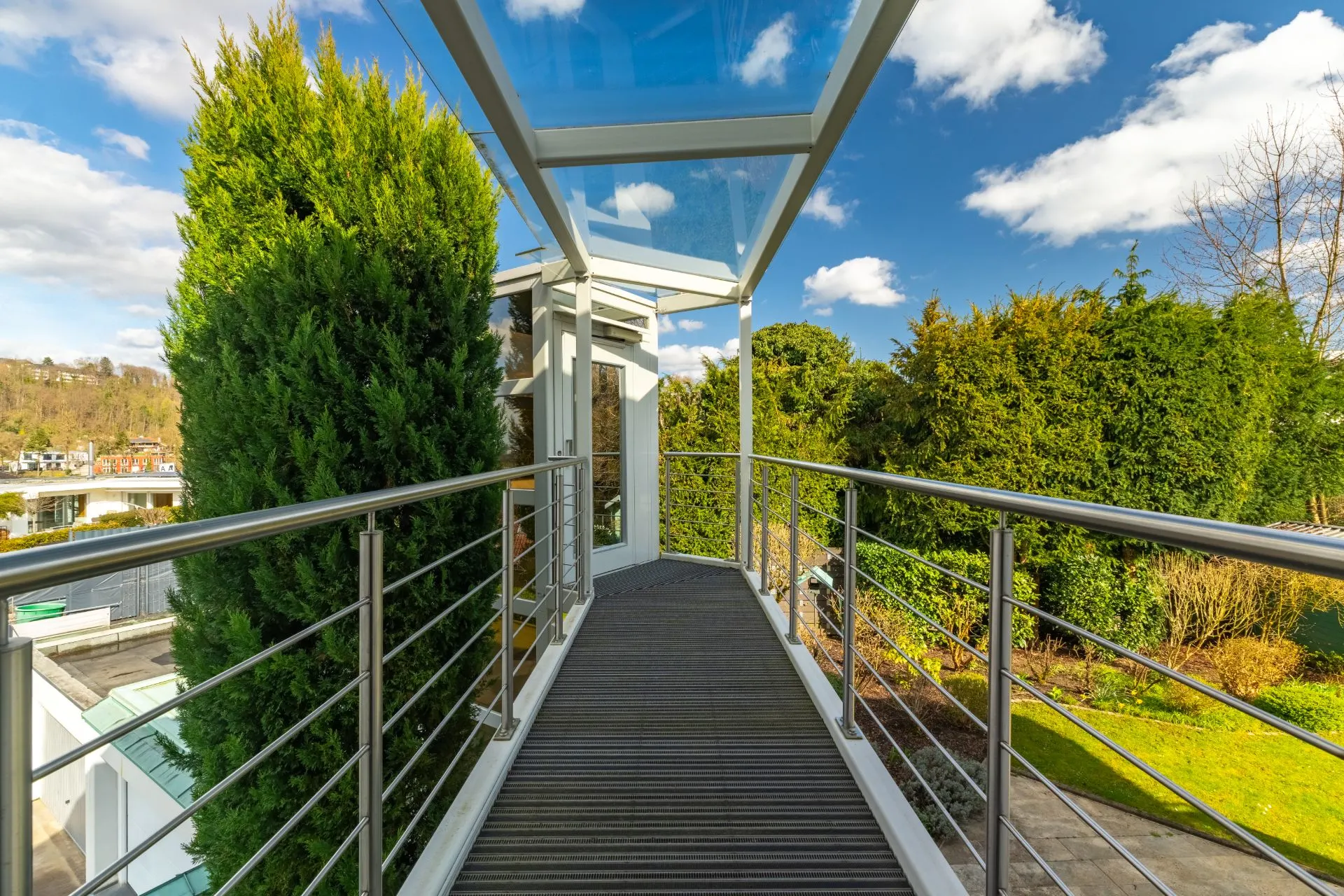 Überdachter Balkon mit Metallgeländer, umgeben von Bäumen und Garten.