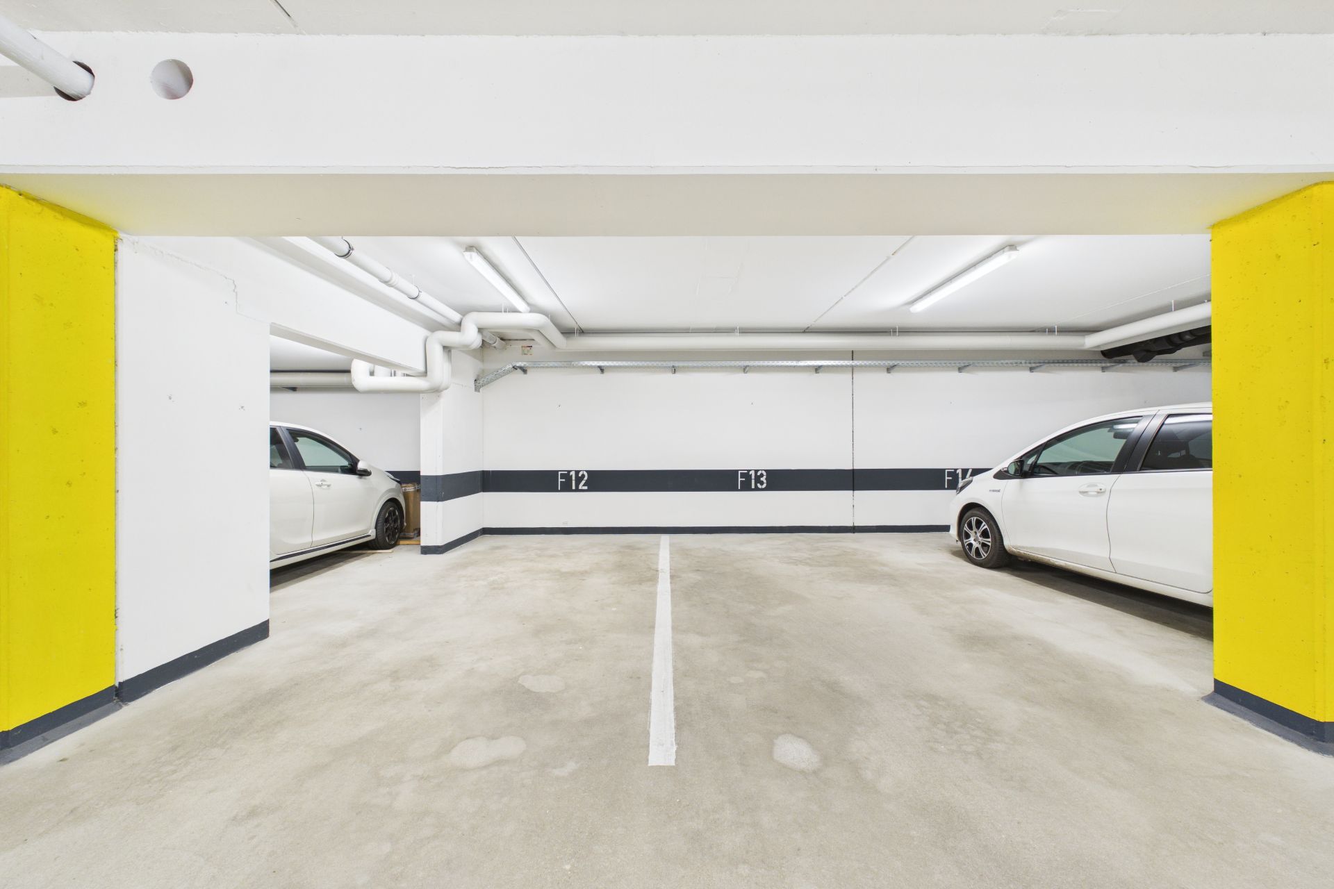 Tiefgaragenstellplatz mit zwei weißen Autos, gelben Säulen und markierten Parkplätzen.