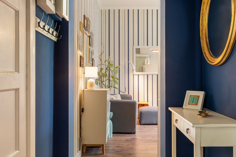 Flur mit dunkelblauen Wänden, kleinem weißen Tisch und Blick ins Wohnzimmer mit gestreifter Wand.