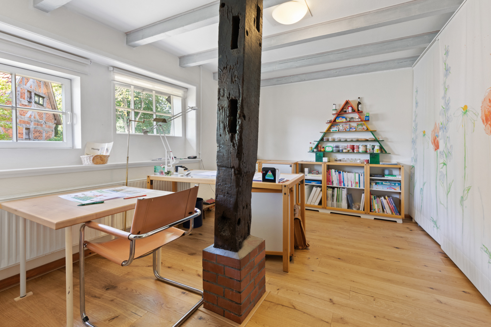 Helles Arbeitszimmer mit Schreibtischen, Holzfußboden, Regal und großen Fenstern.