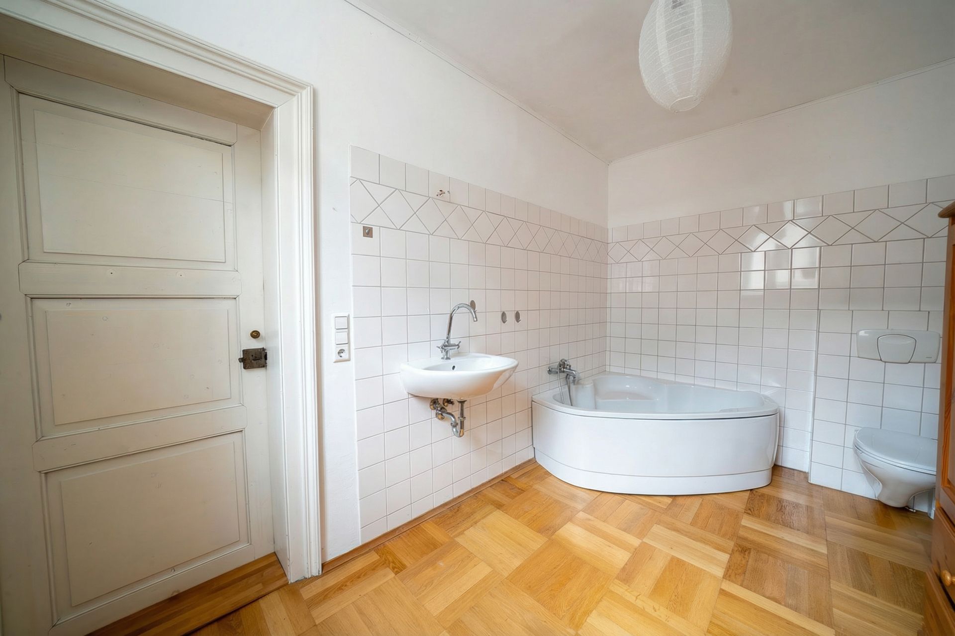 Helles Badezimmer mit Eckbadewanne, Waschbecken, Toilette und Holzboden.