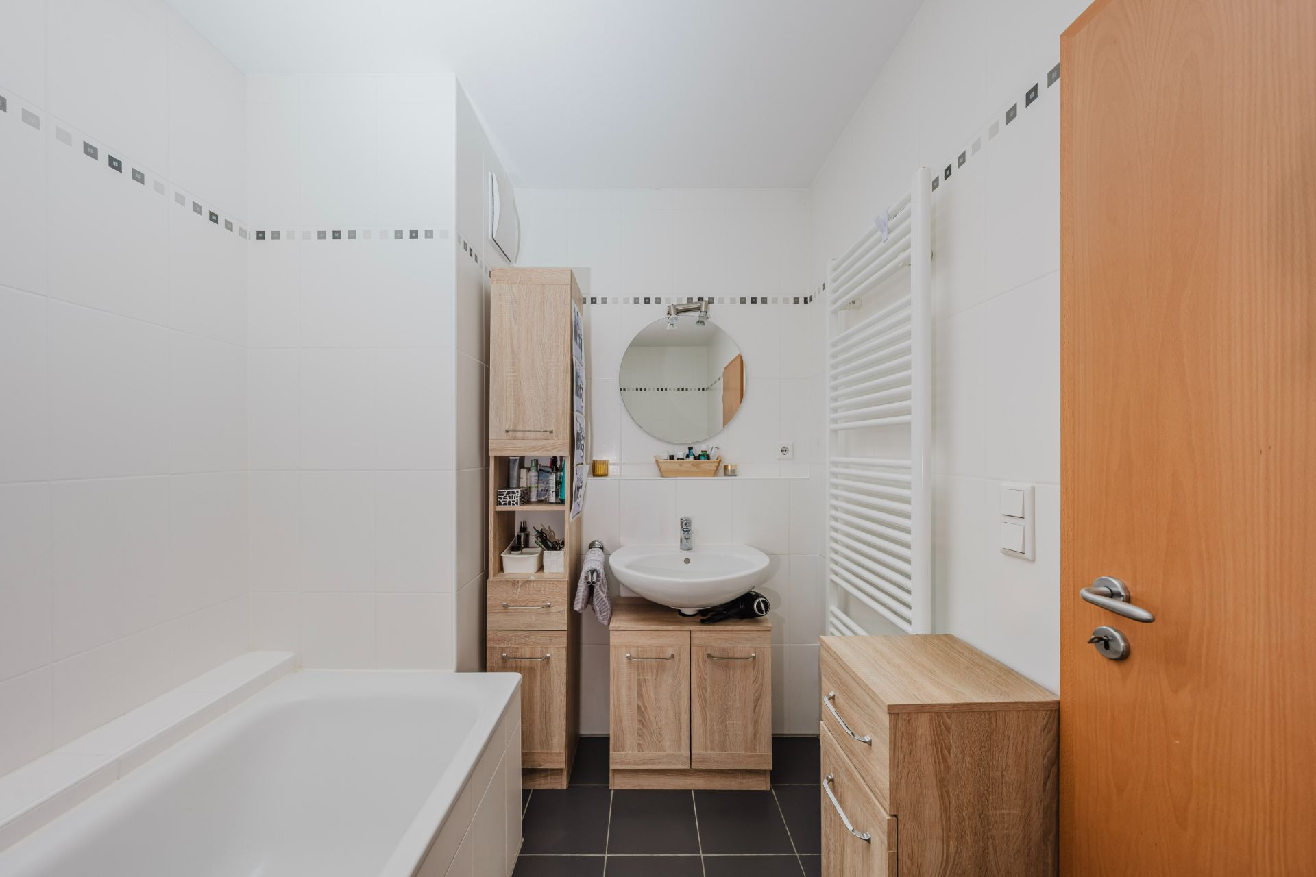 Helles Badezimmer mit Badewanne, Waschbecken, Holzschränken und Handtuchheizkörper.