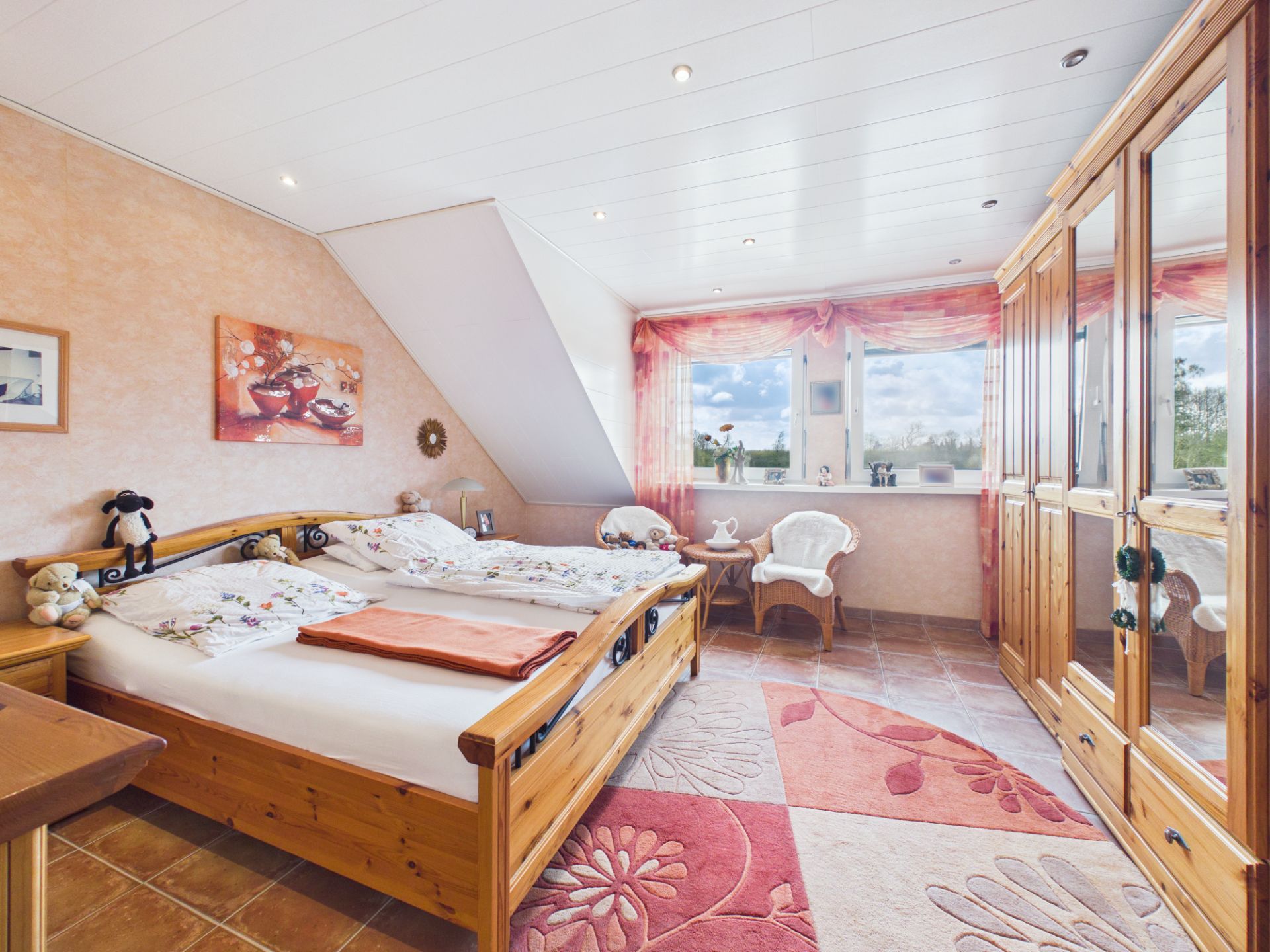 Helles Schlafzimmer mit Doppelbett, großem Kleiderschrank und zwei Fenstern mit rosa Vorhängen.