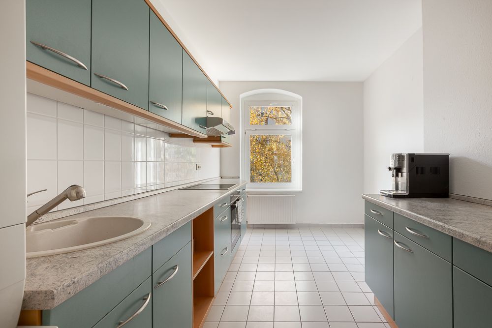 Moderne Küche mit grünen Schränken, weißem Fliesenboden und Fenster mit Blick nach draußen.