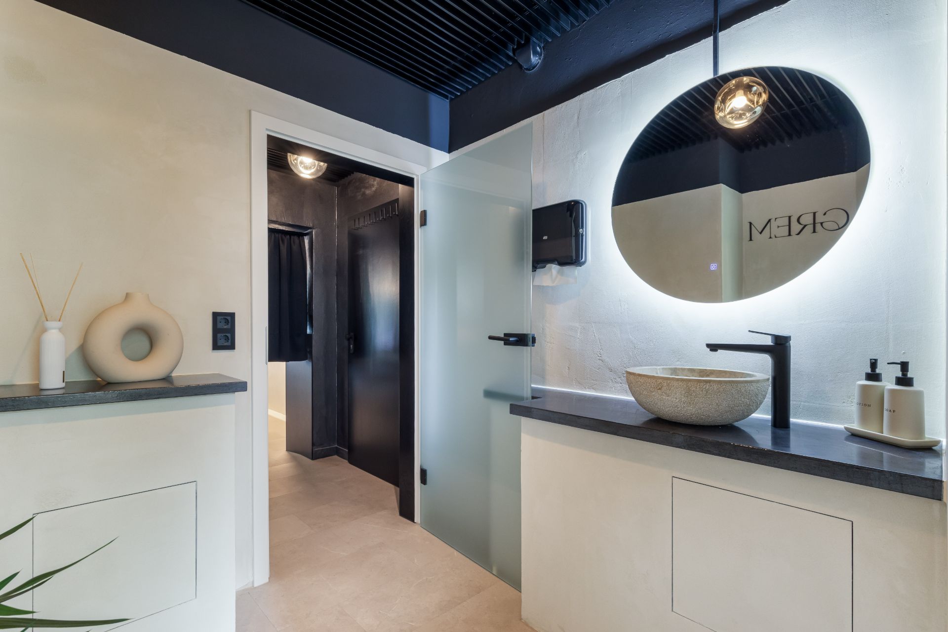 Modernes Badezimmer mit rundem Spiegel, Aufsatzwaschbecken und schwarzem Wasserhahn.
