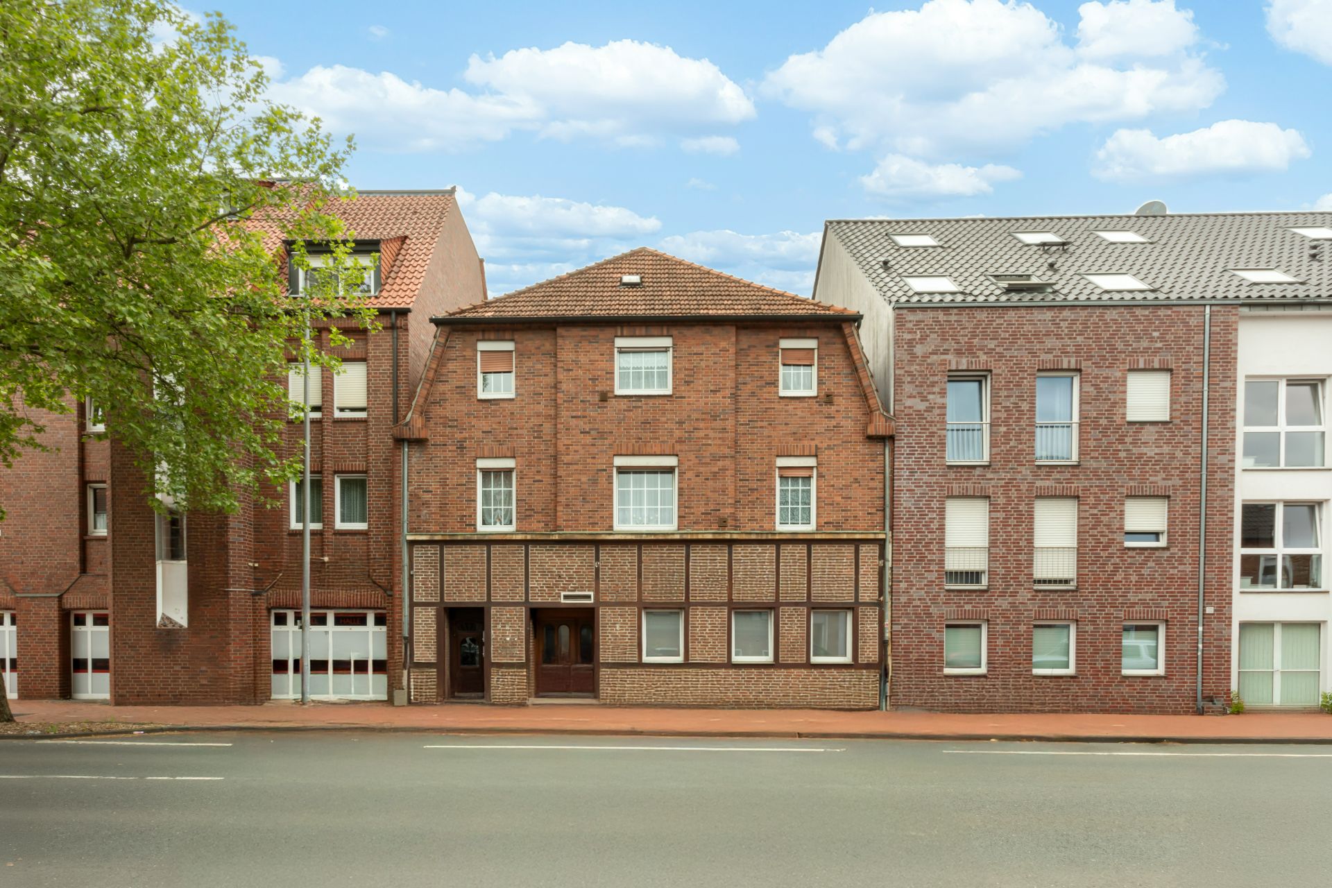 Mehrstöckiges Wohnhaus mit roter Ziegelfassade an einer Straße, umgeben von weiteren Gebäuden.