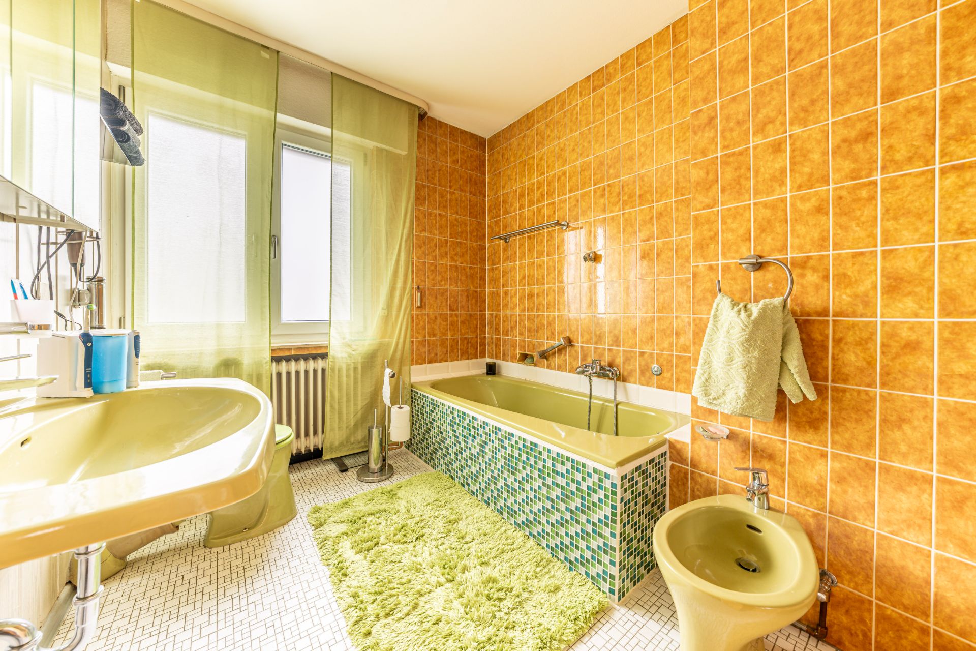 Badezimmer mit grüner Badewanne, orangen Fliesen und grünem Teppich.