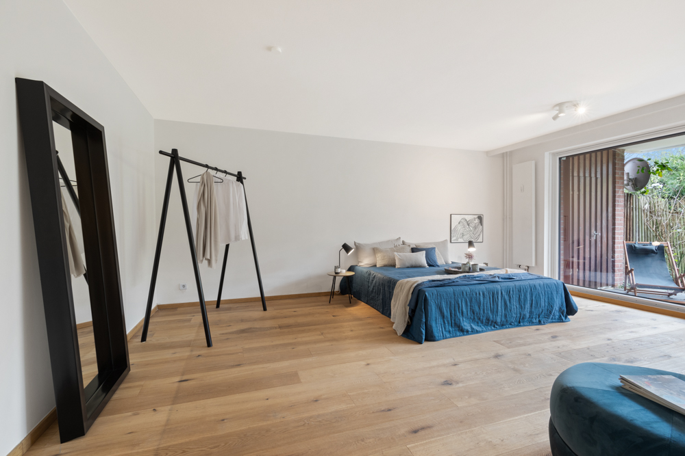 Modernes Schlafzimmer mit großem Bett, Kleiderständer, Spiegel und Zugang zur Terrasse.
