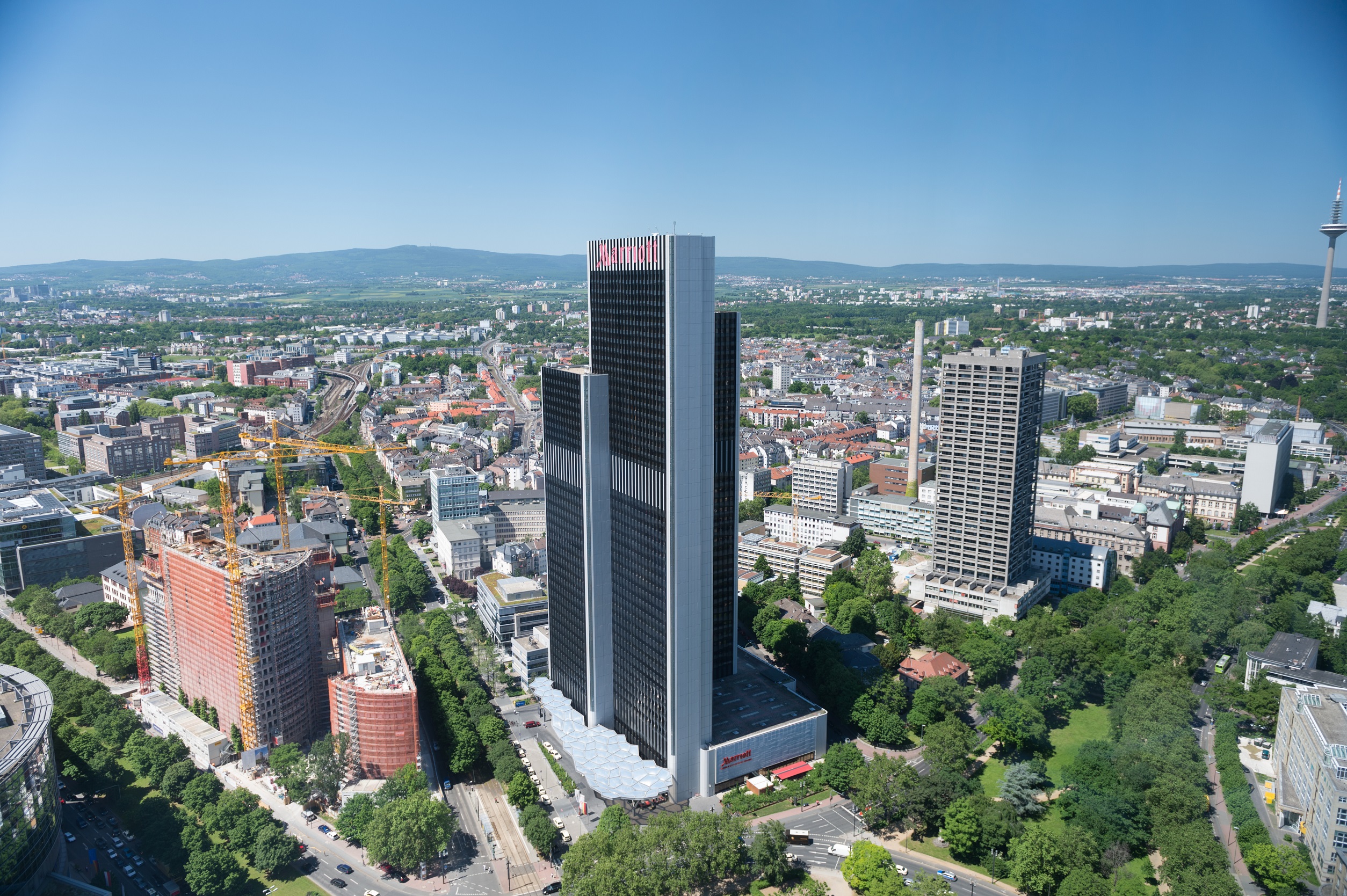 Stadtansicht mit hohen Bürogebäuden, Baustellen und viel Grün im Vordergrund.