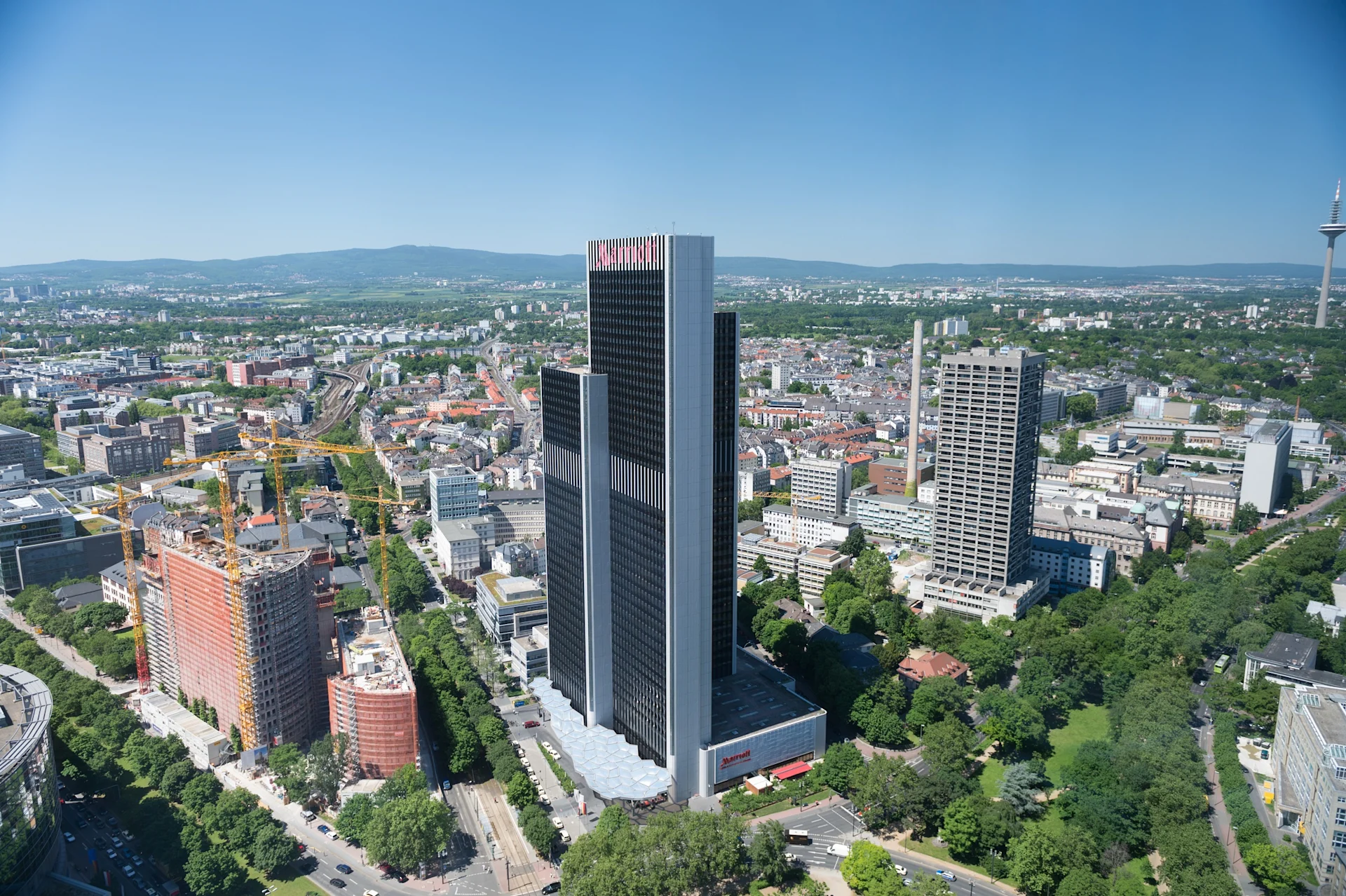 Stadtansicht mit hohen Bürogebäuden, Baustellen und viel Grün im Vordergrund.