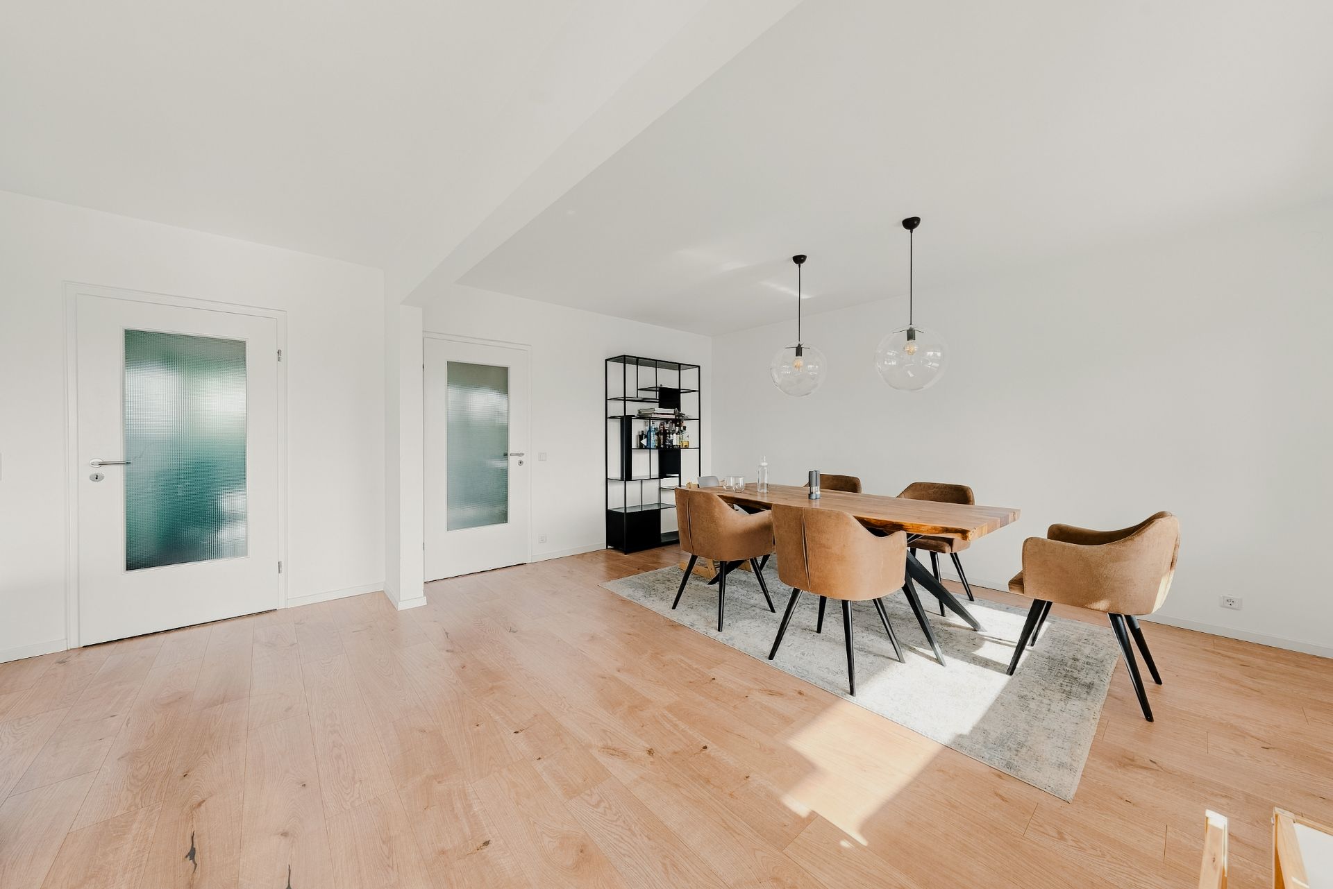 Helles Esszimmer mit Holzboden, Esstisch, sechs Stühlen und Regalen an der Wand.