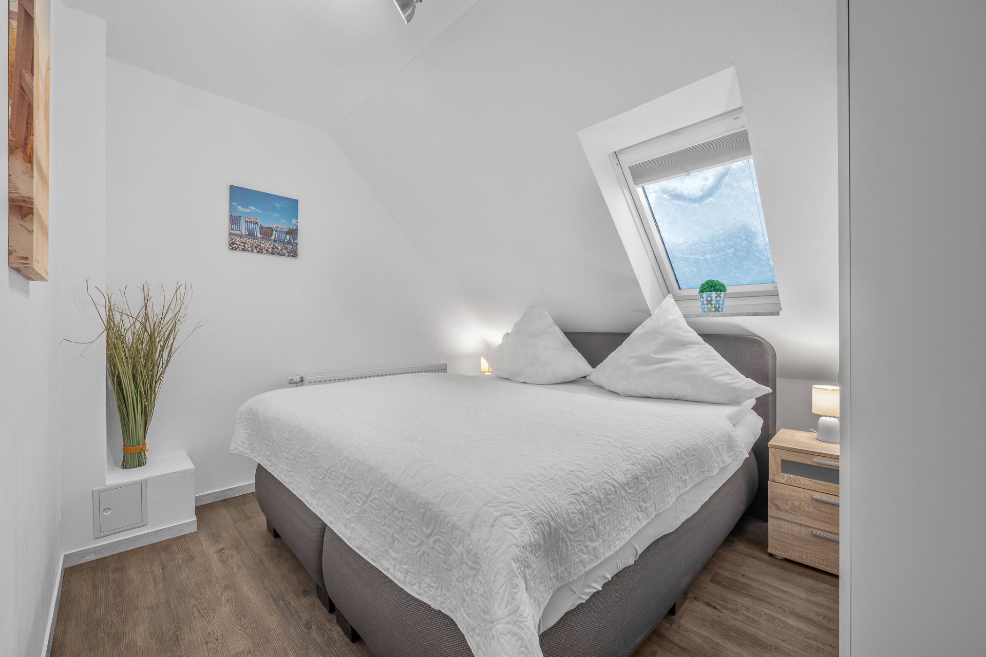 Kleines Schlafzimmer mit Doppelbett, Nachttisch, Lampe und Fenster mit Rollo.
