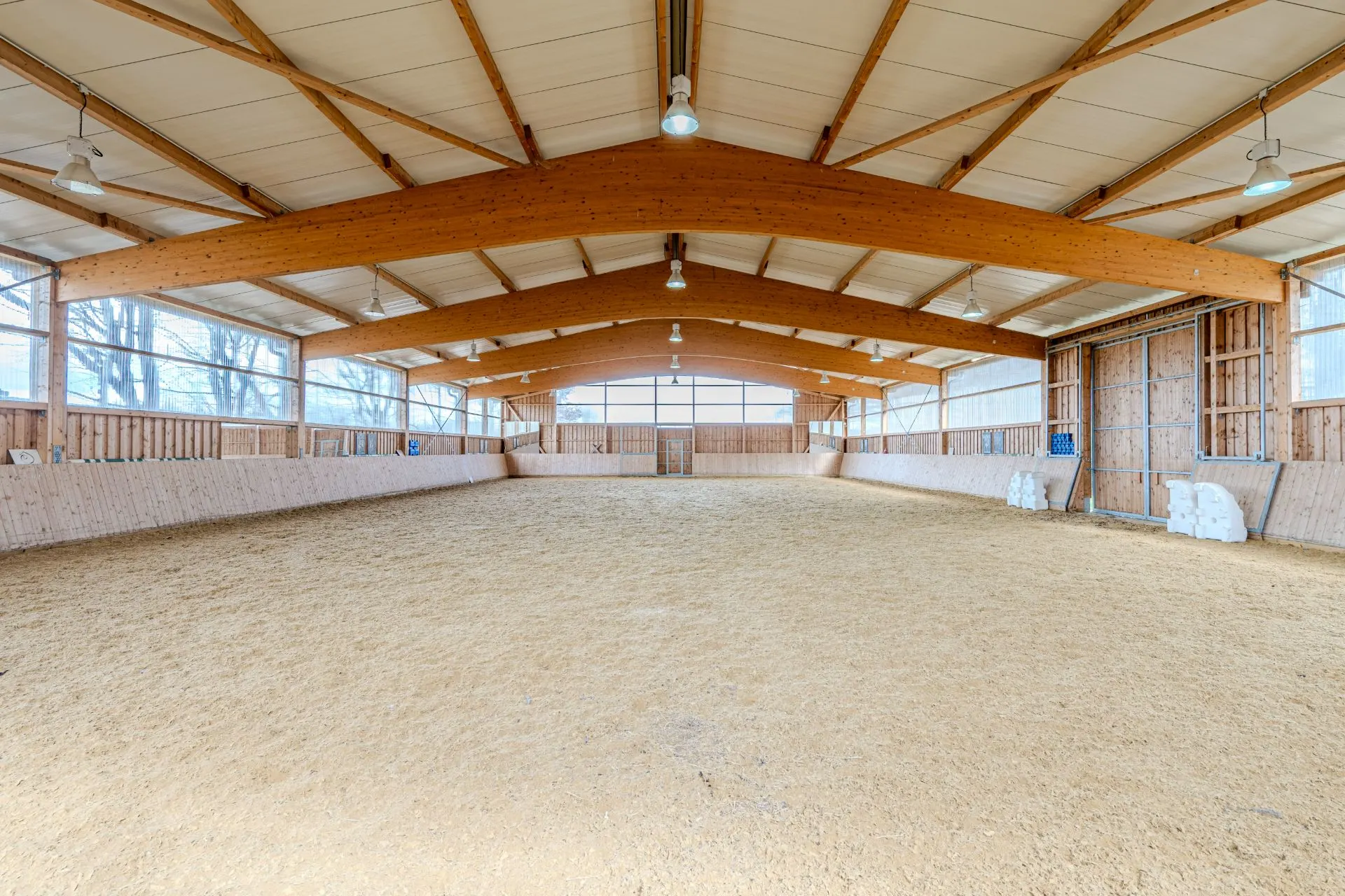 Große, helle Reithalle mit Sandboden und Holzbalken an der Decke.