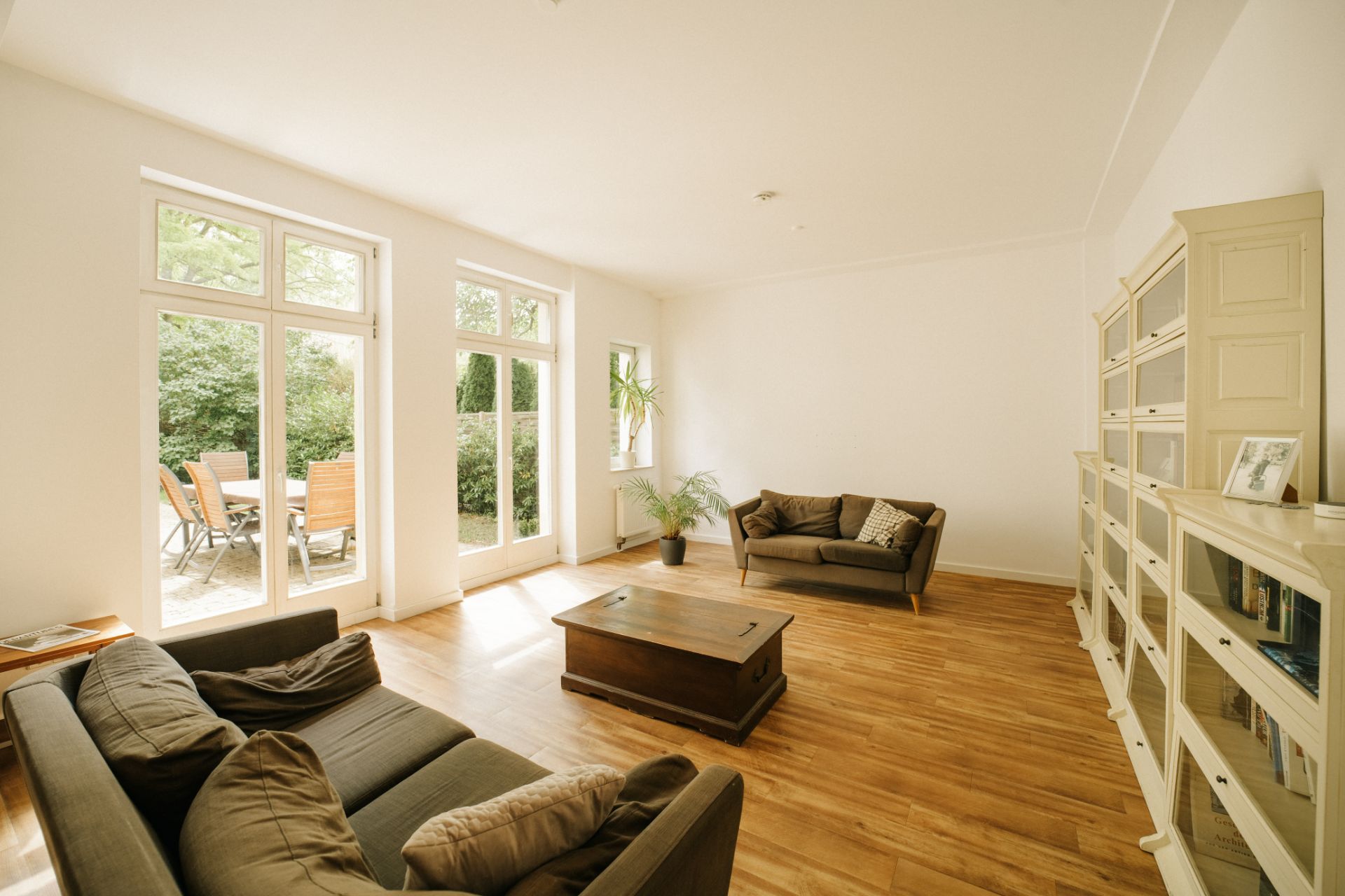 Helles Wohnzimmer mit zwei Sofas, Couchtisch, Bücherregal und Zugang zur Terrasse mit Gartenmöbeln.