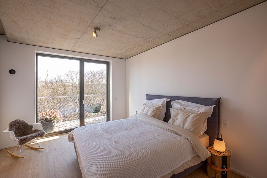 Modernes Schlafzimmer mit Doppelbett, Schaukelstuhl und Zugang zu einem Balkon mit Glasfront.