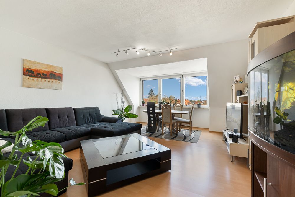 Helles Wohnzimmer mit schwarzem Sofa, Couchtisch, Esstisch am Fenster und Aquarium.