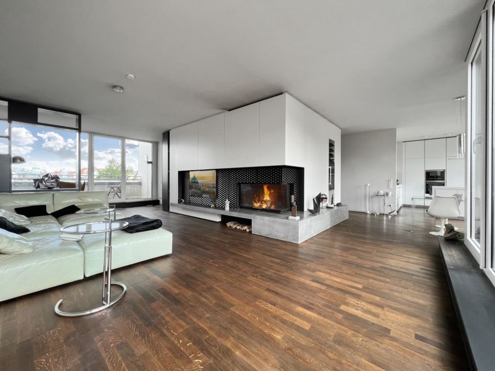 Modernes Wohnzimmer mit Kamin, großer weißer Couch und Holzboden, Fenster mit Blick nach draußen.