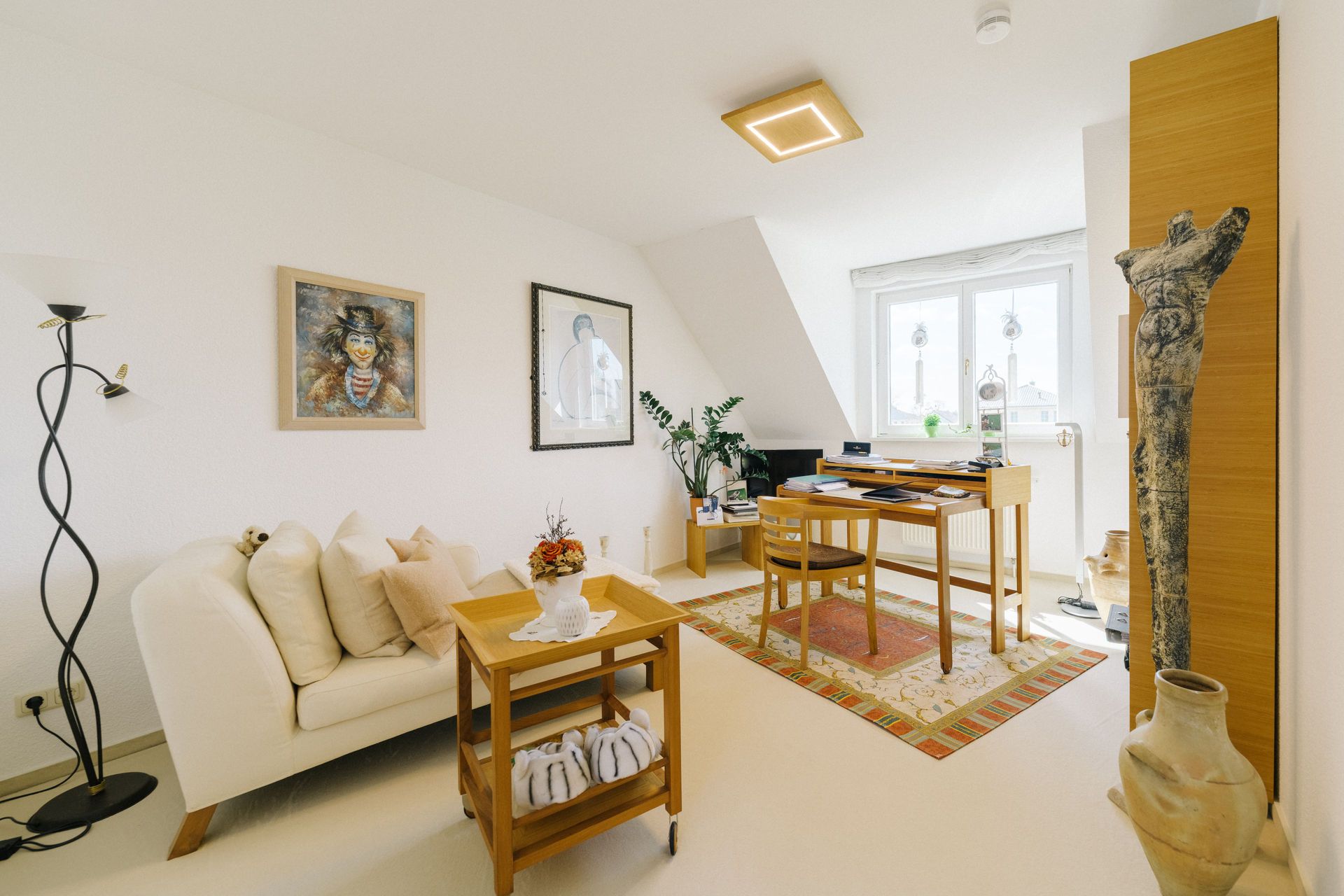 Helles Wohnzimmer mit Sofa, Tisch, Schreibtisch, Stühlen, Kunstwerken und Dekorationen.
