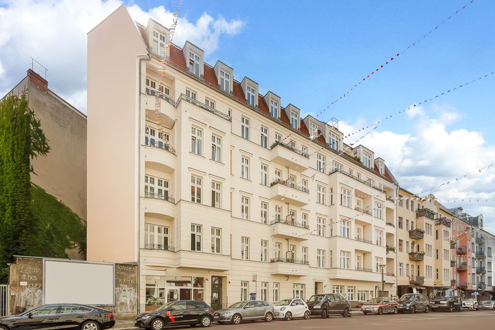 Mehrstöckiges Wohnhaus mit Balkonen an einer Straße, mehrere Autos parken davor.
