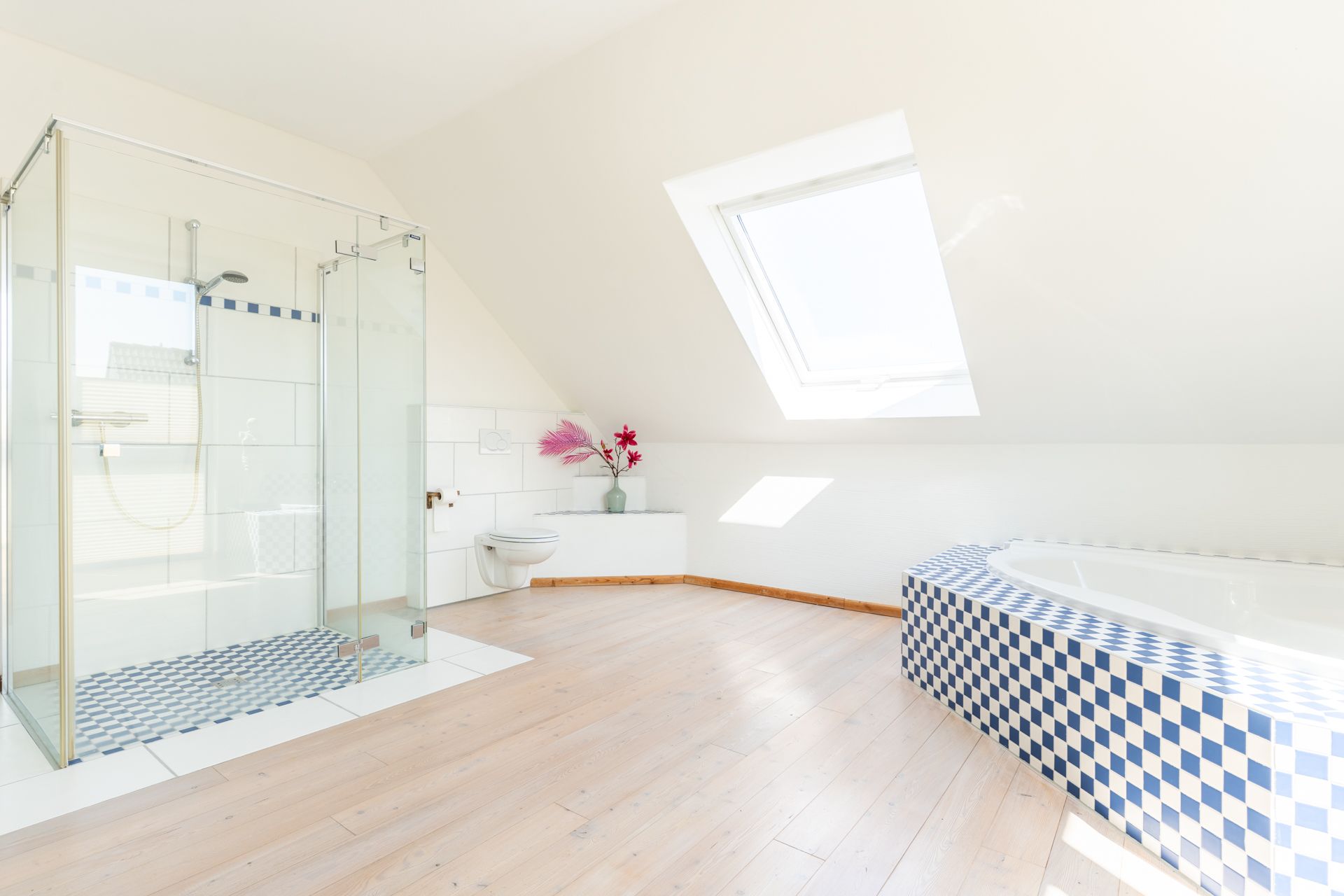 Helles Bad mit Glasdusche, Eckbadewanne mit blauen Fliesen und Dachfenster.