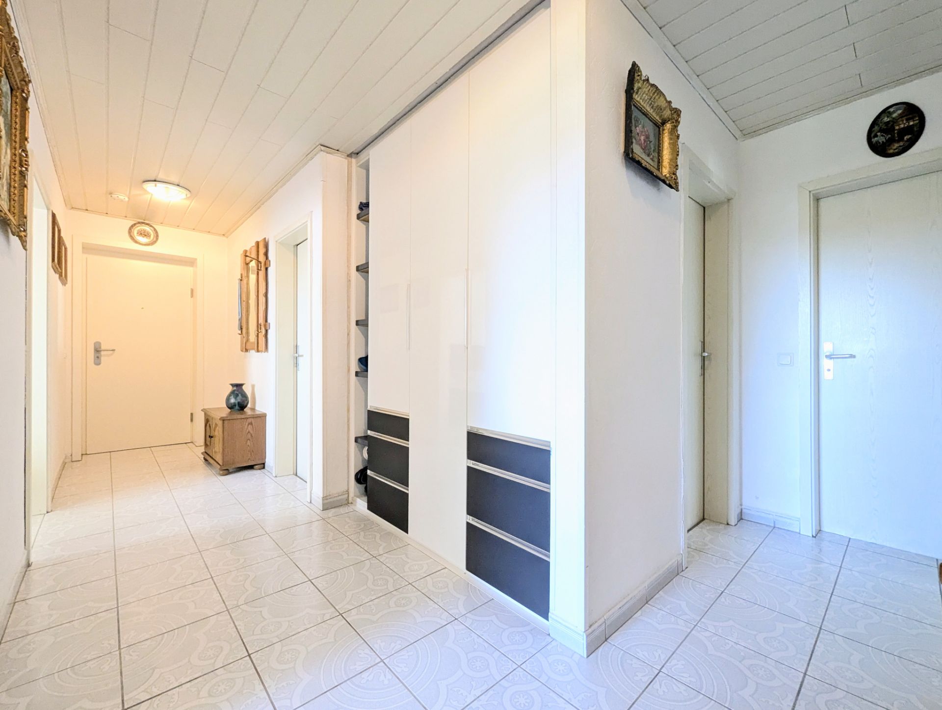 Heller Flur mit weißen Wänden, Türen, großem Einbauschrank und Fliesenboden.